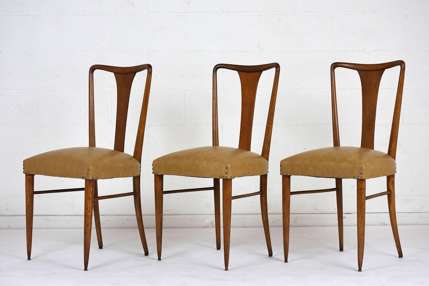 This set of six Modern-style dining chairs feature wood frames stained a light walnut color with a lacquered finish. The seat backs have curved edges and a simple splat. The tapered legs have stretched bars and are finished with brass toe caps. The