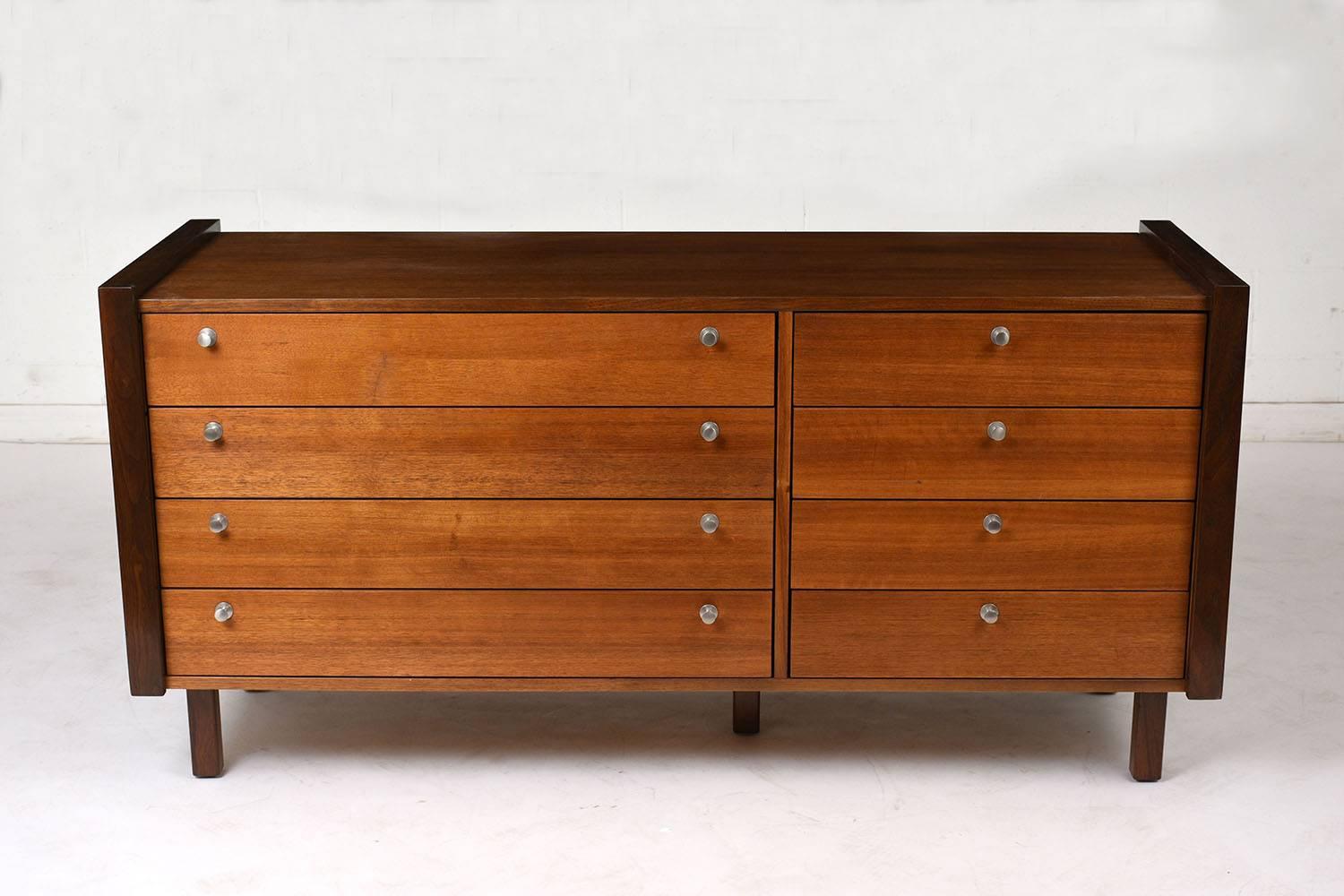 This 1970's Mid-Century Modern-style chest of drawers is made from walnut wood stained in a mid tone walnut color with a polished finish. The chest has eight drawers, four larger drawers on the left and four smaller drawers on the right. The drawers