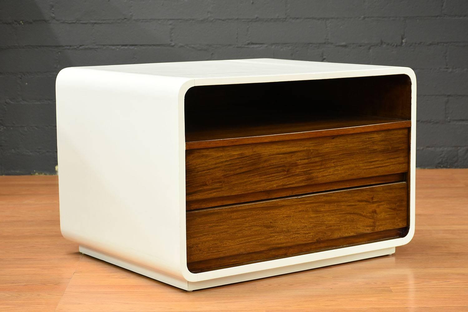 This pair of 1960s Mid-Century Modern-style nightstands is made of walnut wood finished in a two-tone color combination of white and a rich walnut color stain. The outside of the nightstands is painted a clean white color and features rounded