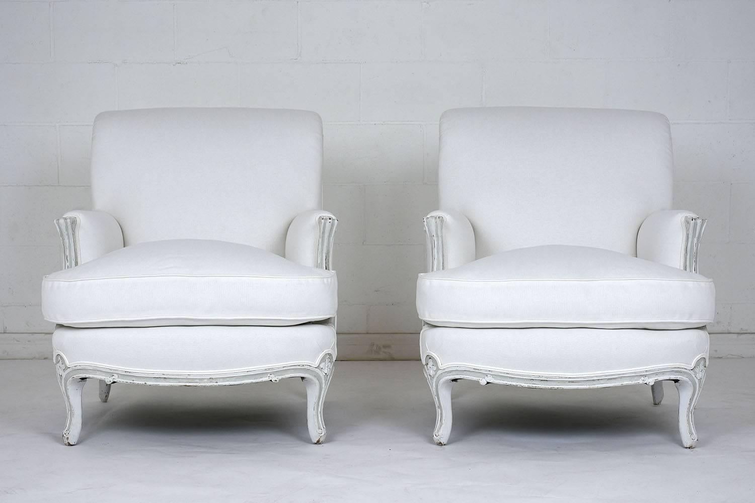 This comfortable pair of 1900's French Louis XV-style bergeres have recently been professionally upholstered in a white linen with double piping trim details. There is a single cushion on the extra deep seat with feather inserts. The carved walnut