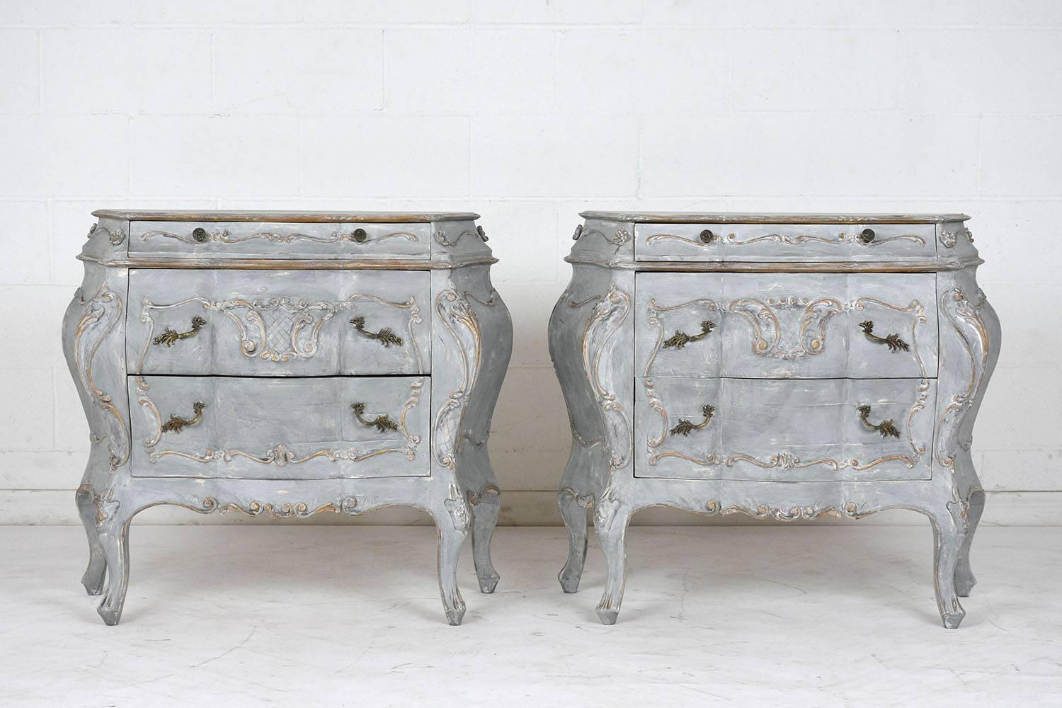 This pair of 1950's Louis XV-style Commodes are crafted out of maple wood and have newly painted in a pale gray & off-white color combination with gilt details. The commodes feature french motif carvings of scrolls, acanthus leaves, quilted