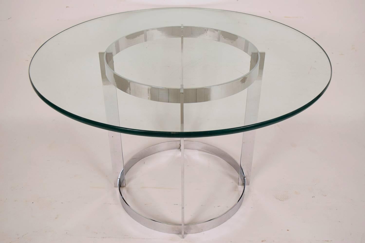 This elegant Mid-Century Modern-style Dining table is equipped with a chrome circular base. The sleek chrome frame is in the shape of a geometrical cylinder. The center table has a thick circular glass that rests upon the base. This center table is