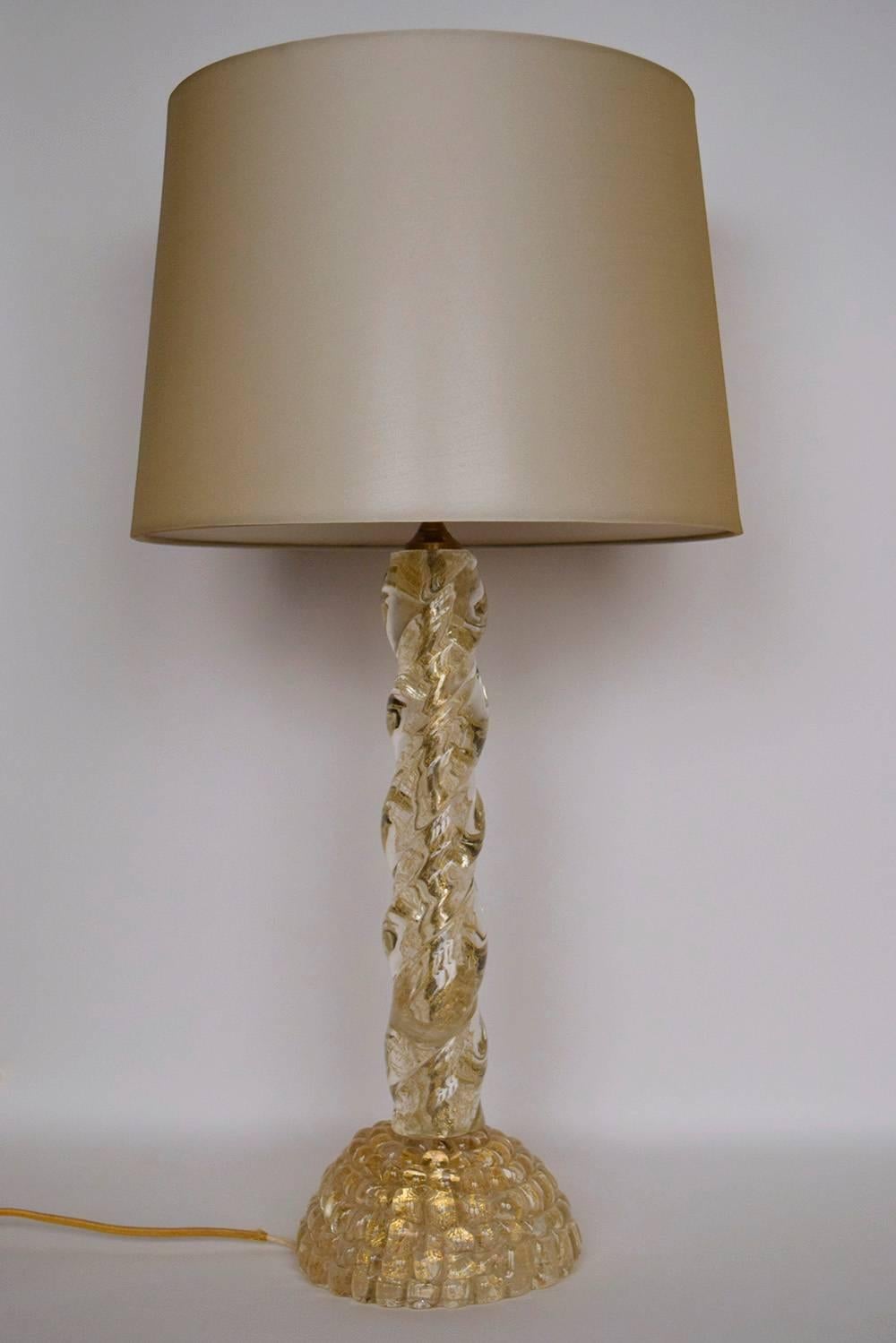 This beautiful pair of Murano-style table lamps feature a twisted-column with a dome design base made of Murano glass. Both lamps feature see-through glass with gold accent specks inside of the thick Murano glass. These lamps are wired to US