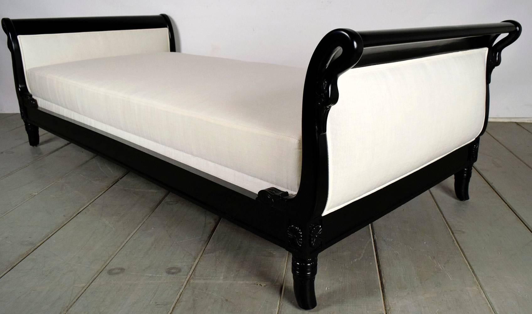 Elegant Empire daybed. Solid mahogany wood frame newly finished in a rich black color. Scroll design headboards with swan carvings. Newly upholstered headboards with double piping trims and new cushion in an ivory color linen fabric all done by a