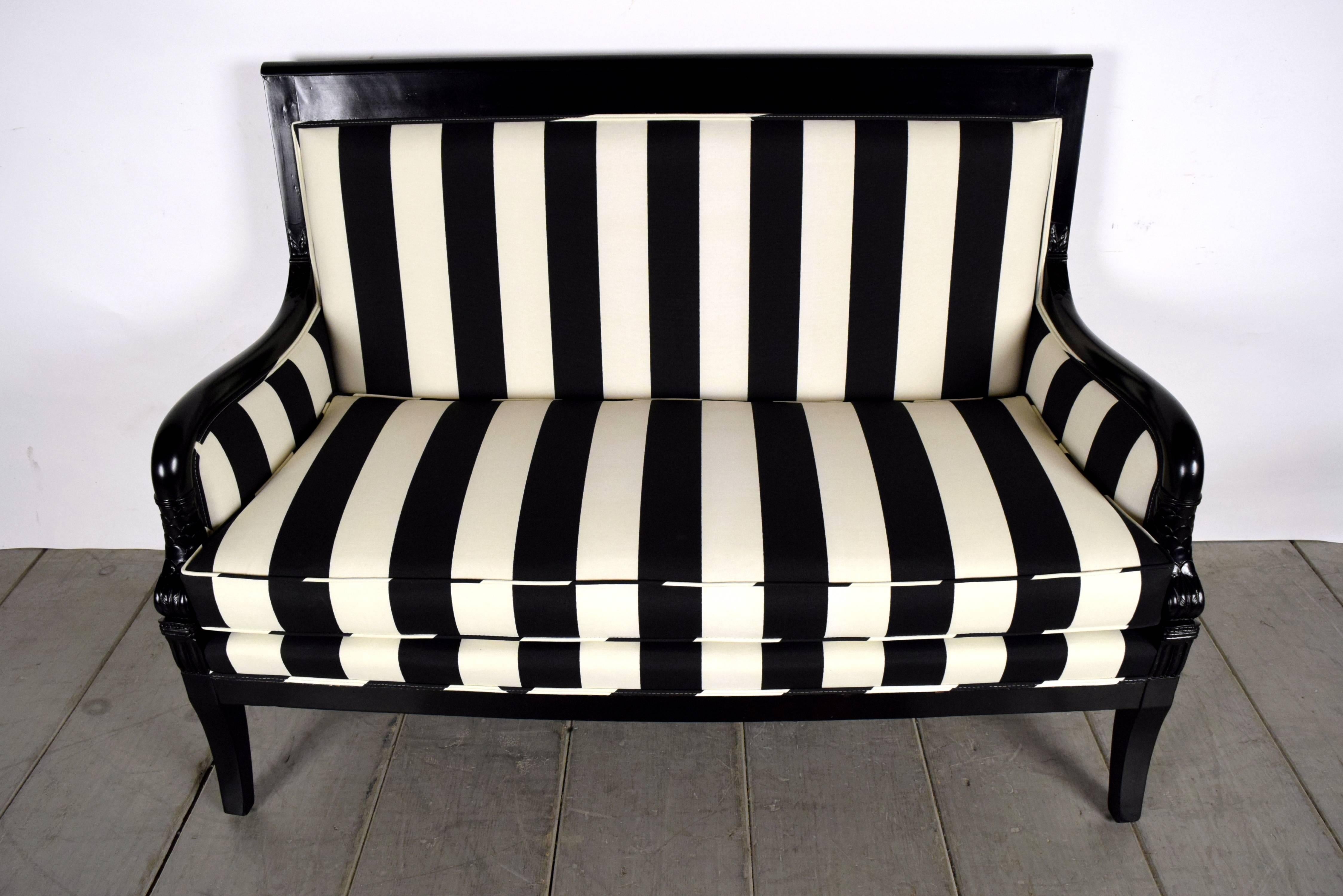 This elegant 1900's Empire-style settee or sofa features a solid wood frame that has been refinished in a rich black lacquered color. On each arm there is a carved depiction of  sea fish and rosettes above the front legs. The seat cushion has been