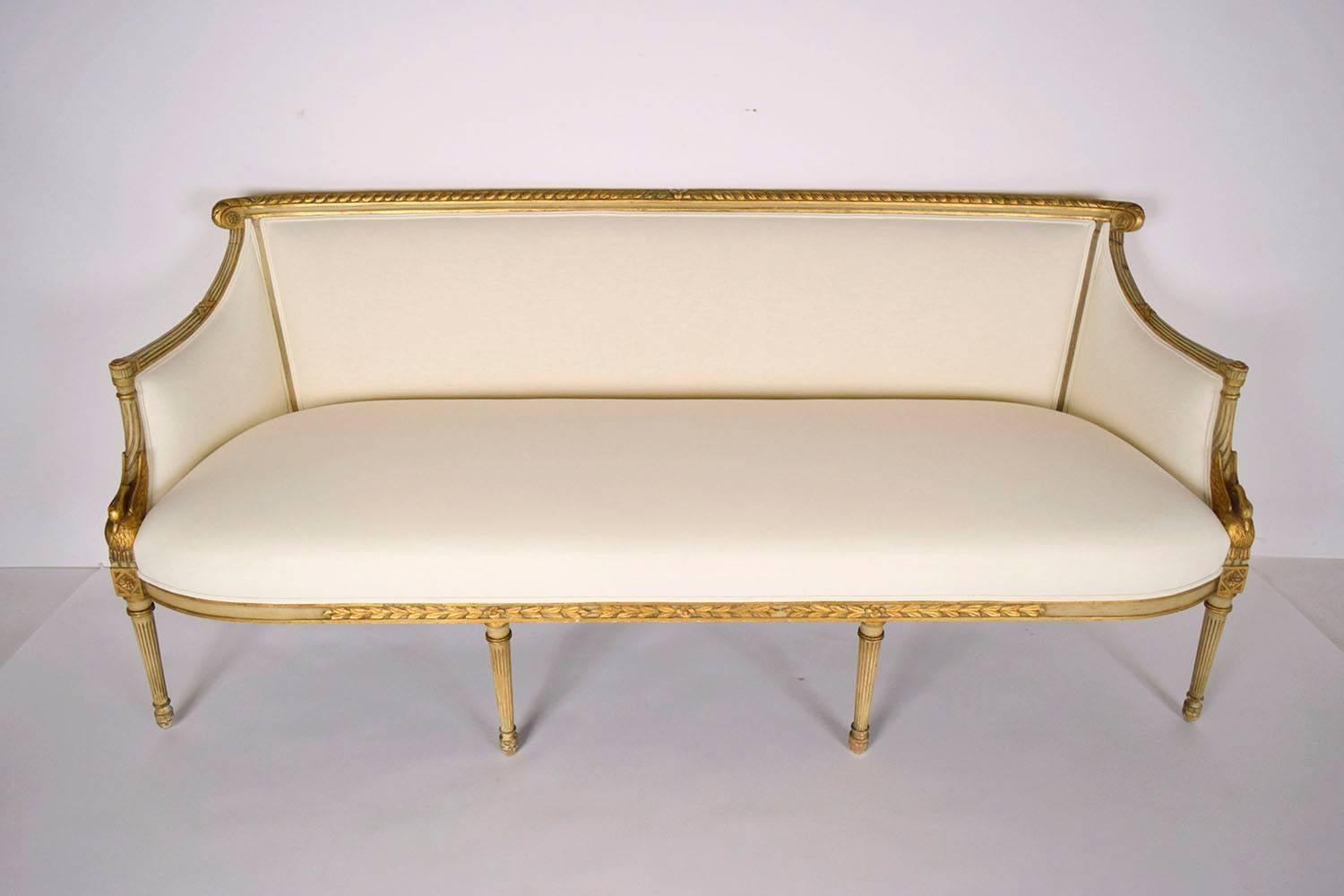 This one of a kind 1890's French Empire sofa features a solid wood frame with its original paint and a gilt finish. There are beautiful carvings throughout the frame with a laurel leaf trim, a swan resting at the bottom each arm, rosettes at the top