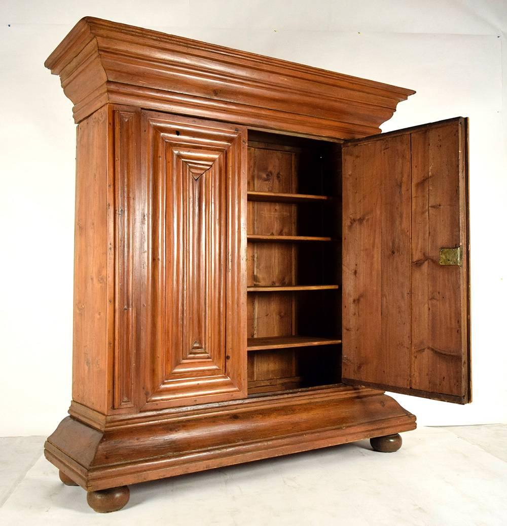 This large 1880's German Schrank armoire is made from solid pine wood with its original light walnut color stain finish. The armoire features large carved moulding on top and two doors with moulding paneling design on their facade. The left side