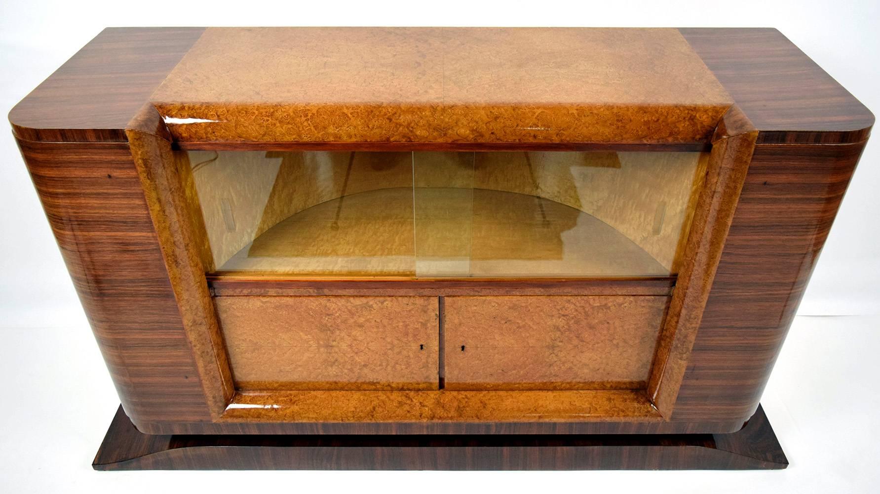 This 1930s French Art Deco-style dry bar or sideboard is made of mahogany wood with a mahogany color stain on the sides and the center is covered in burl wood veneers in a golden yellow color stain. The sideboard is finished with a high gloss