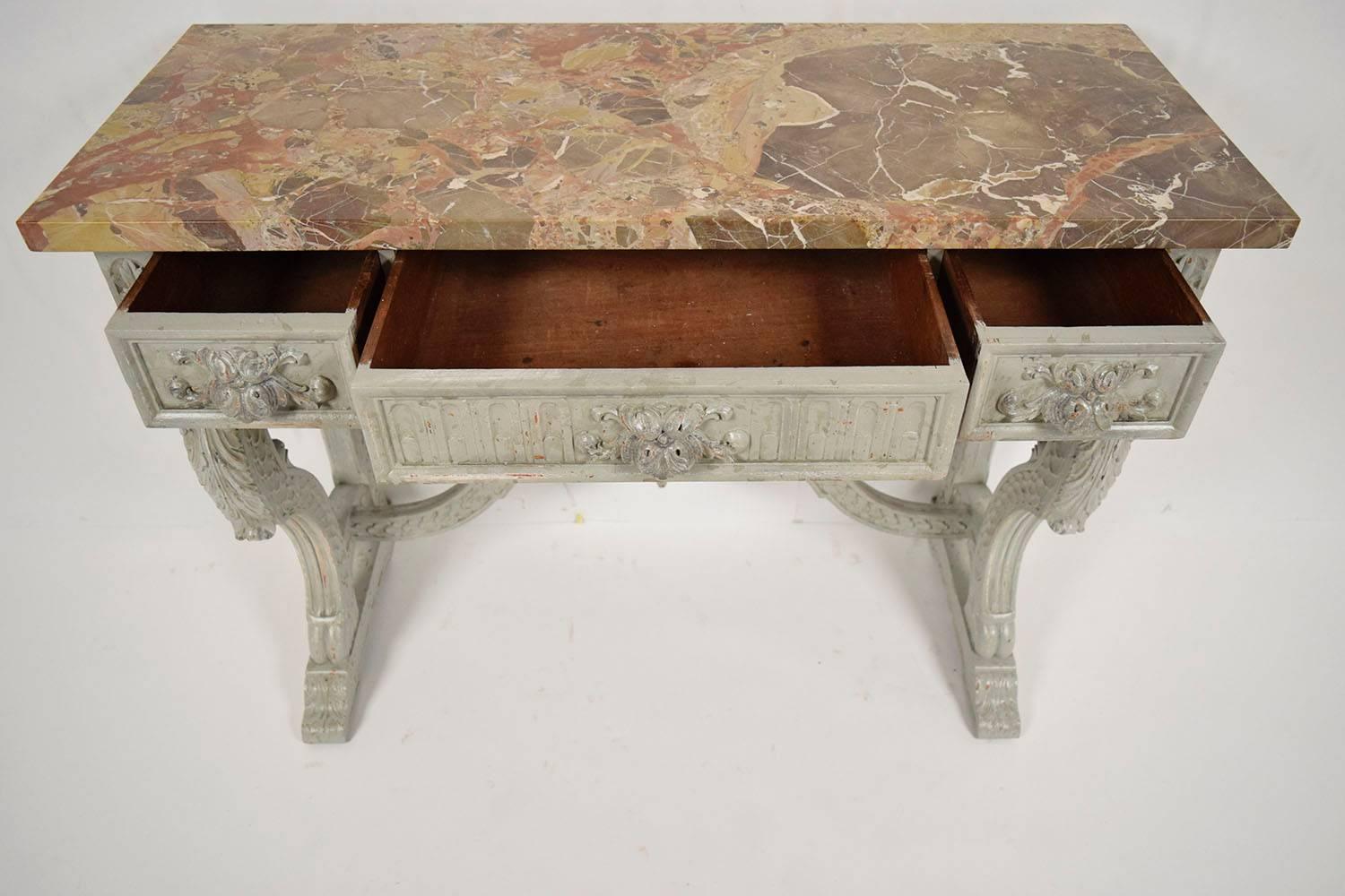 This is a 1890s French console in Louis XVI style. Has a thick multicolored marble top. Solid walnut wood, newly painted in a light gray color with a distressed finish. Frame is heavily carved with, flowers, scrolls, leaves, and sea shells. The top
