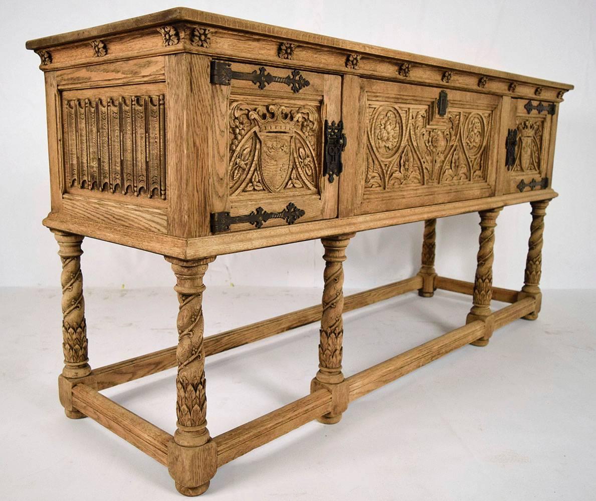 This is a 1900s French sideboard in Spanish Colonial style. Solid oakwood, that has been bleached to show its natural color. Has a wooden top with an elegant carved trim and rosettes under the top. Three front doors with iron hinges and locks. The