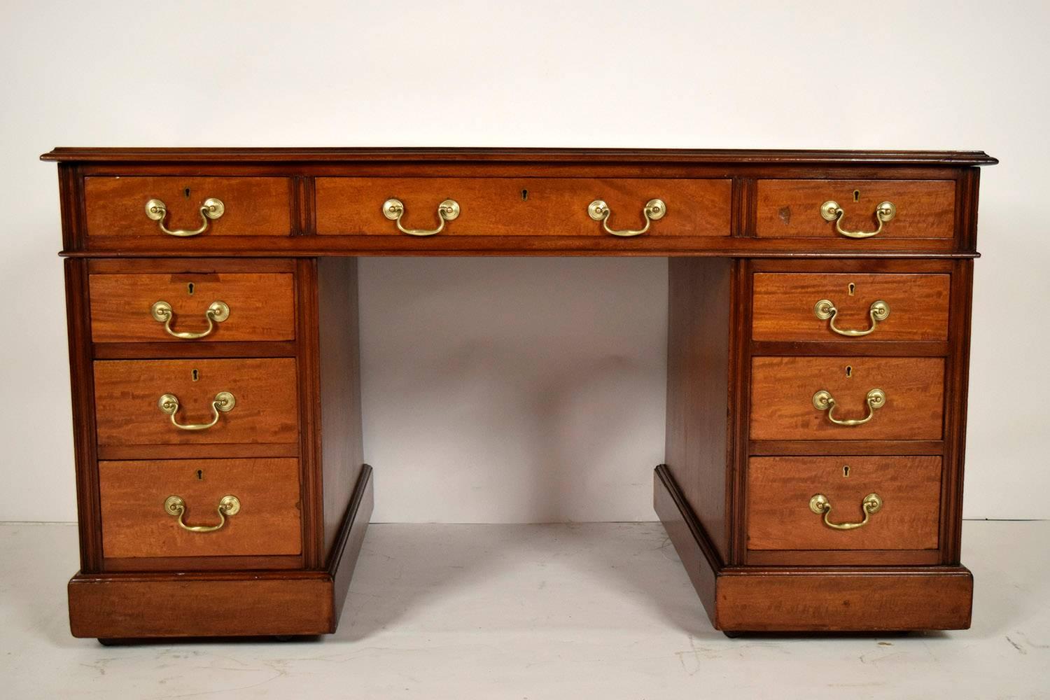 Elegant English pedestal desk. Original brown embossed leather top, solid wood finished in a mahogany color. Features one large center drawer with dual brass handles, each side has four drawers with single brass handles. Key and locks are in great