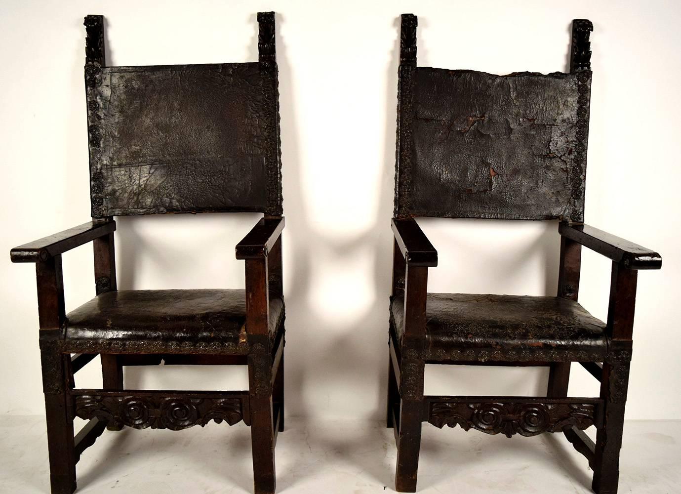 This Pair of 1750's Spanish Colonial Throne Chairs are made out of walnut wood with its original dark walnut finish and are in good condition. The seat & backrests are covered in the original leather with floral brass nailhead details and the pair