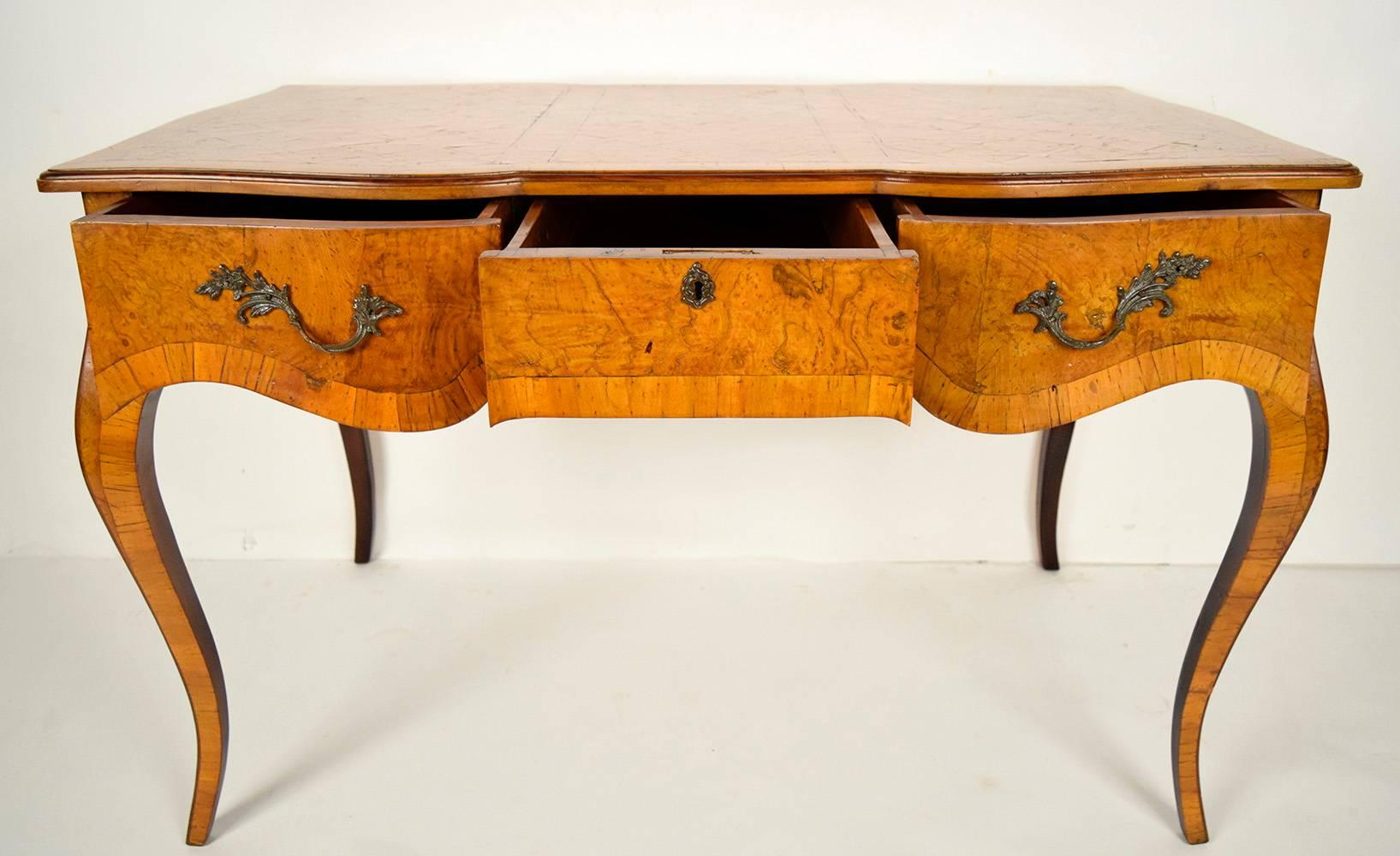 This is a 1900s Louis XV-style desk made from solid wood with beautiful marquetry decorations on top and inlaid burl and walnut veneers on the sides and legs with its original golden finish. The front of the desk has three side by side drawers with