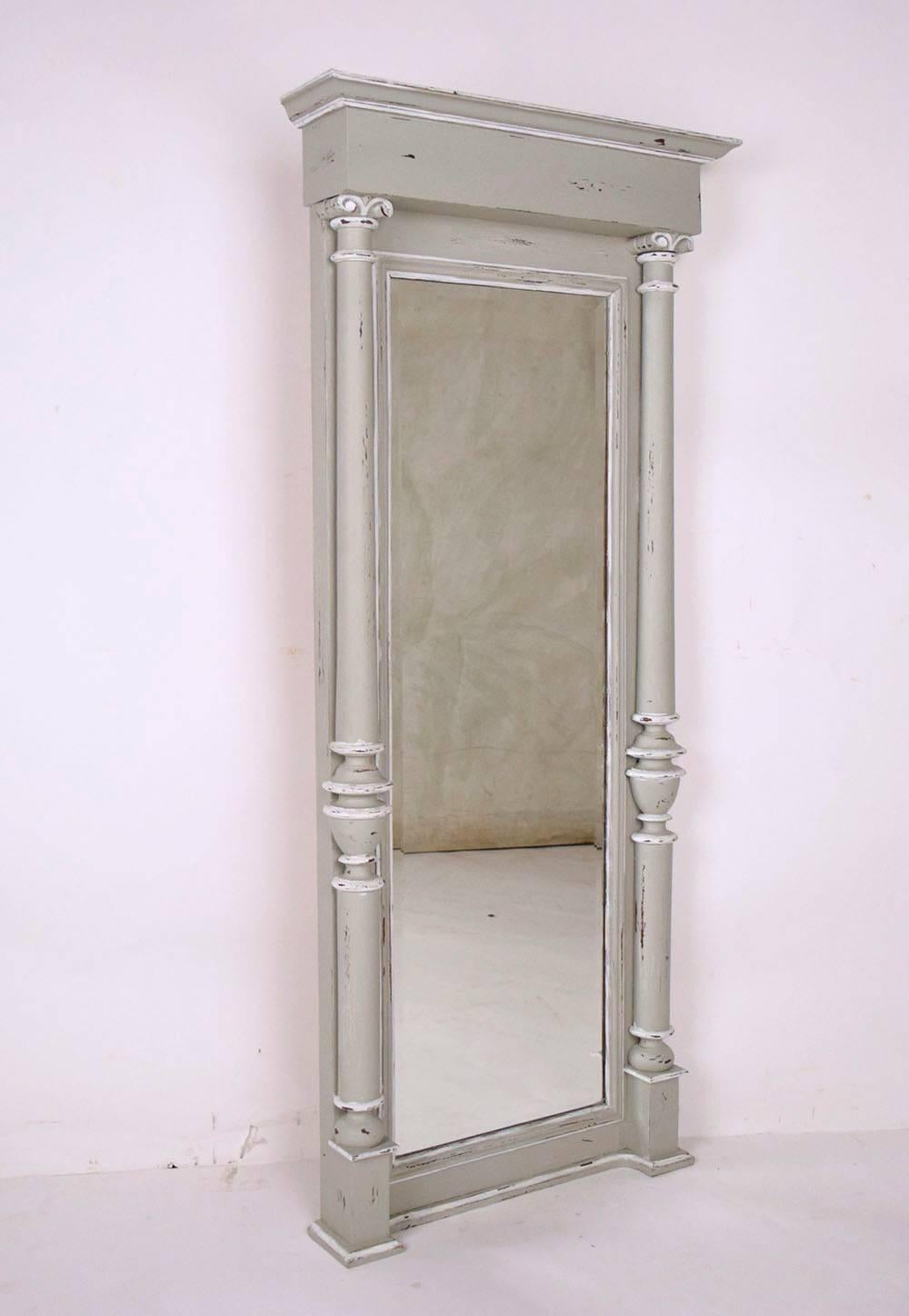 This 1900's French Empire-style standing wall mirror features a solid mahogany wood frame that has been recently painted in a gray and oyster combination with a distressed finish. This full size mirror is elegantly designed using architectural