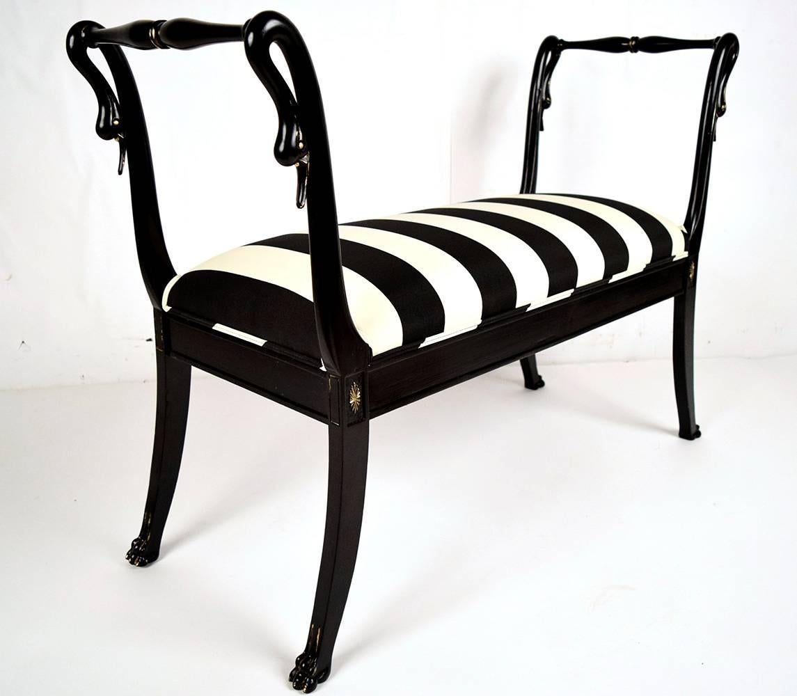 Beautiful 1900s Empire French bench. Solid mahogany wood frame, newly finished in a rich elegant black lacquered color with gilt accents. Has carved swan heads, on the arms, followed by a newly upholstered seat in a black and ivory stripe fabric