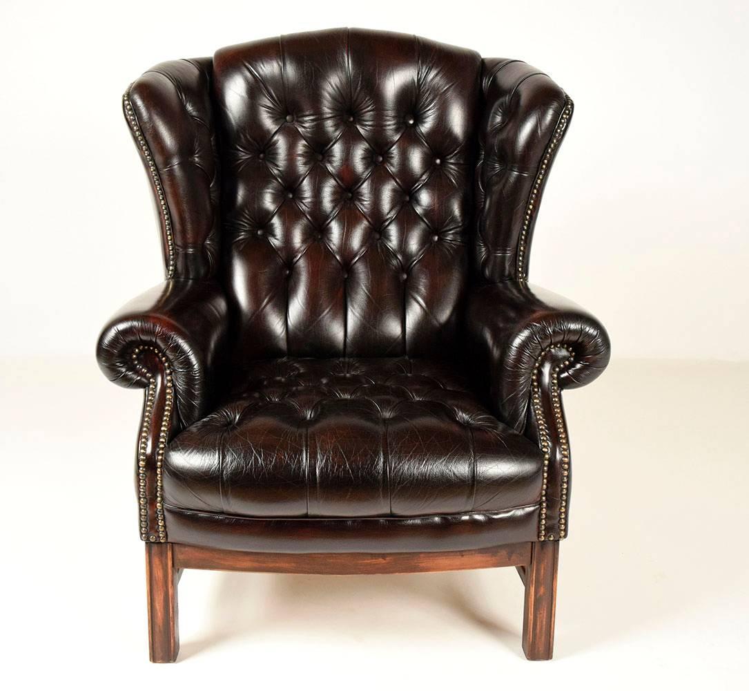 Single 1960s wing back tufted leather chair. Solid mahogany wood frame, wing back, scroll arms, comfortable seat, all in a dark brown leather, that is tufted on the back, wings and seat. Has nailhead decoration on the front wings and front of the