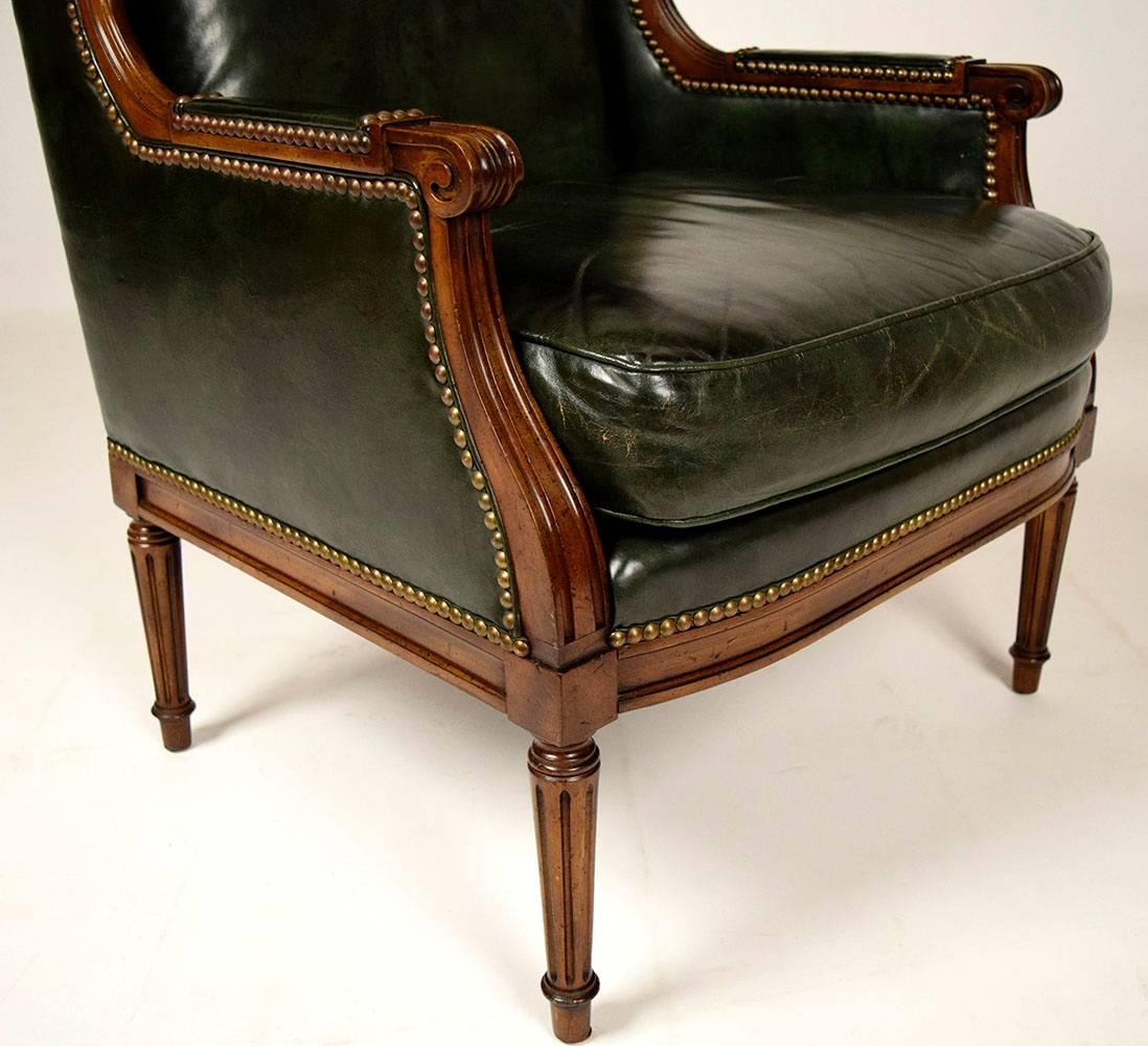 Elegant 1960s Louis XVI style wingback chair. Solid maple wood carved frame, original dark walnut color finish. Upholstered in original dark green leather color, seat has single foam cushion. Nail heads decorate the whole frame, finished with carved