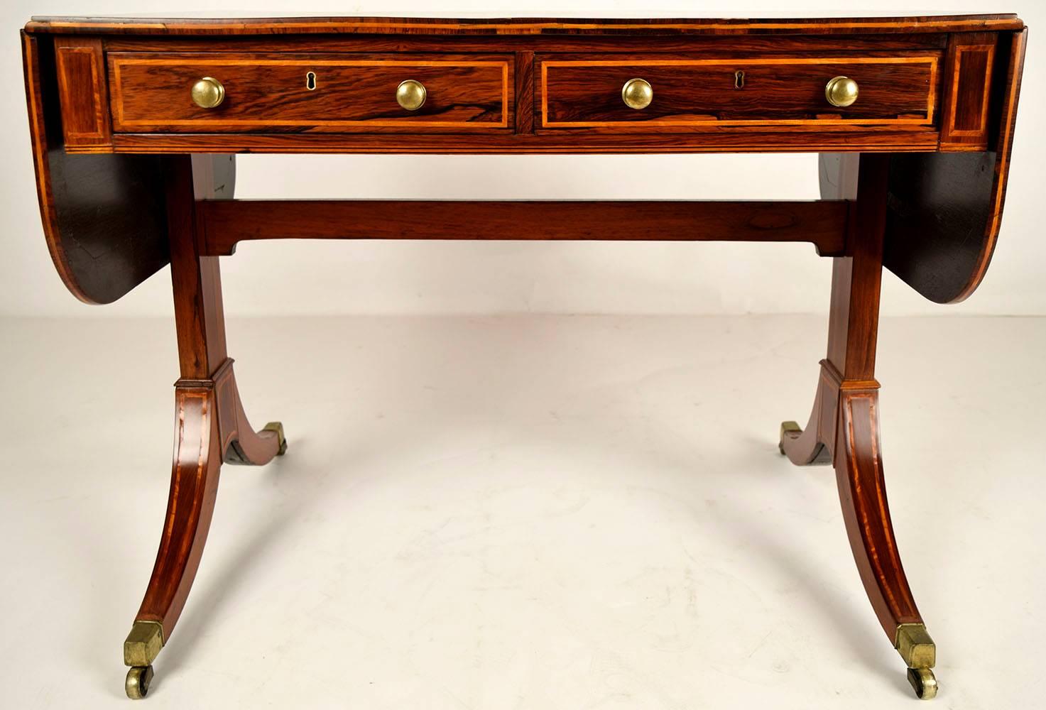 This is a 1870s English sofa table. Mahogany wood was used to make this beautiful desk, has two side leaves that lift up to make it longer. Has elegant inlaid design all throughout the top, sides, front and legs. Features two front drawers with deal