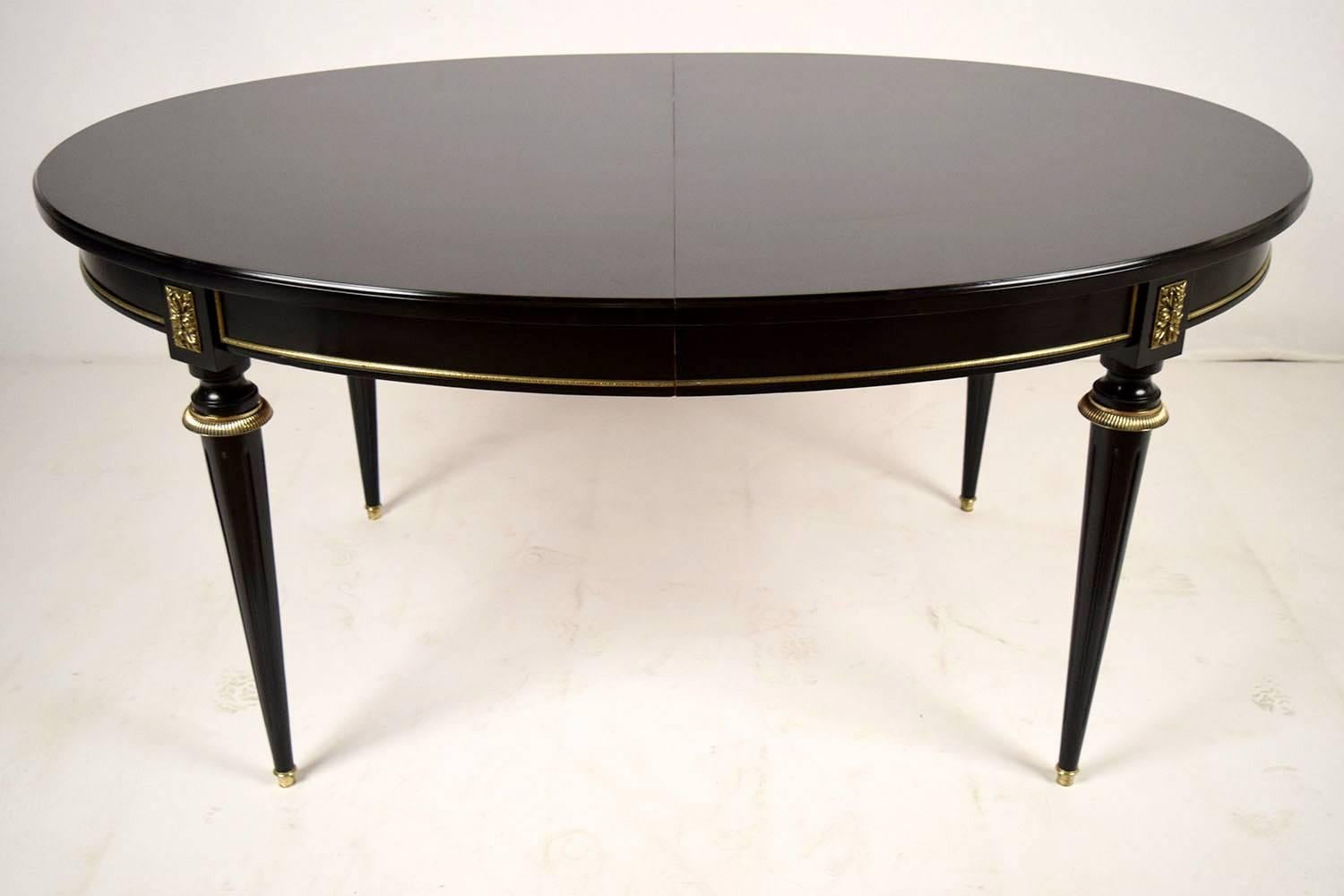 This 1910's French oval dining table is made of solid mahogany wood that has been finished using an ebonizing technique in a deep black color. Along the bottom edge of the table are brass mouldings and accents in each corner and along the long