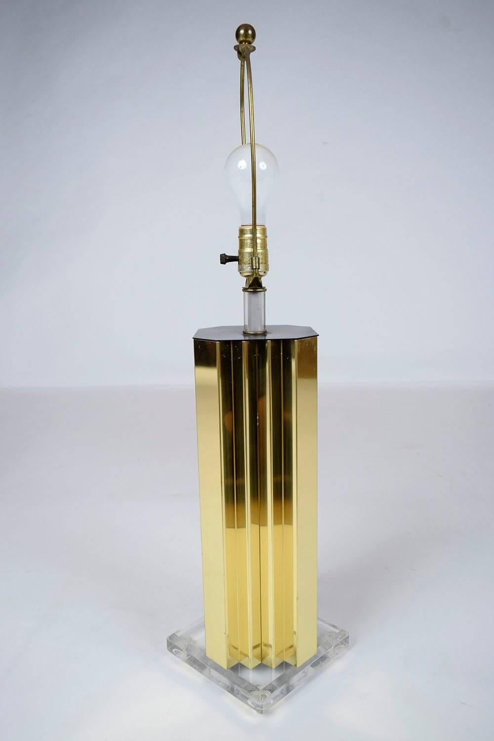 This single 1970's Mid Century Table Lamp is a statement piece that is sure to light up any room. The eye-catching geometric brass lamp pedestal sits atop a clear lucite base and comes with a new white fabric lampshade that complements the angles of