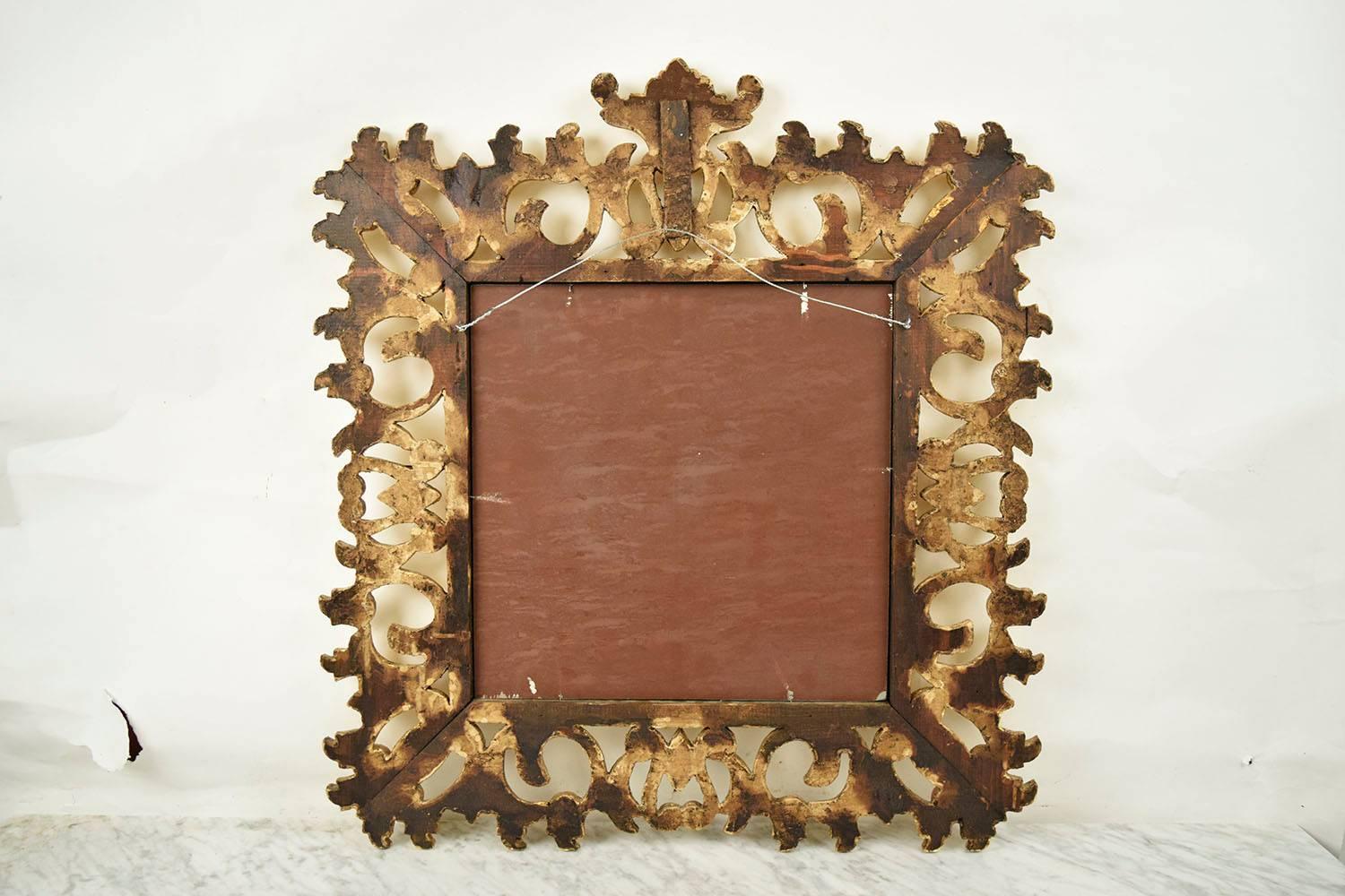 This Ornate 1950's Italian Baroque-style Wall Mirror features a giltwood frame with floral motif carvings covering the square carved frame. The heavily carved frame is attached to the mirror by a simple boarder around the mirror. This elegant