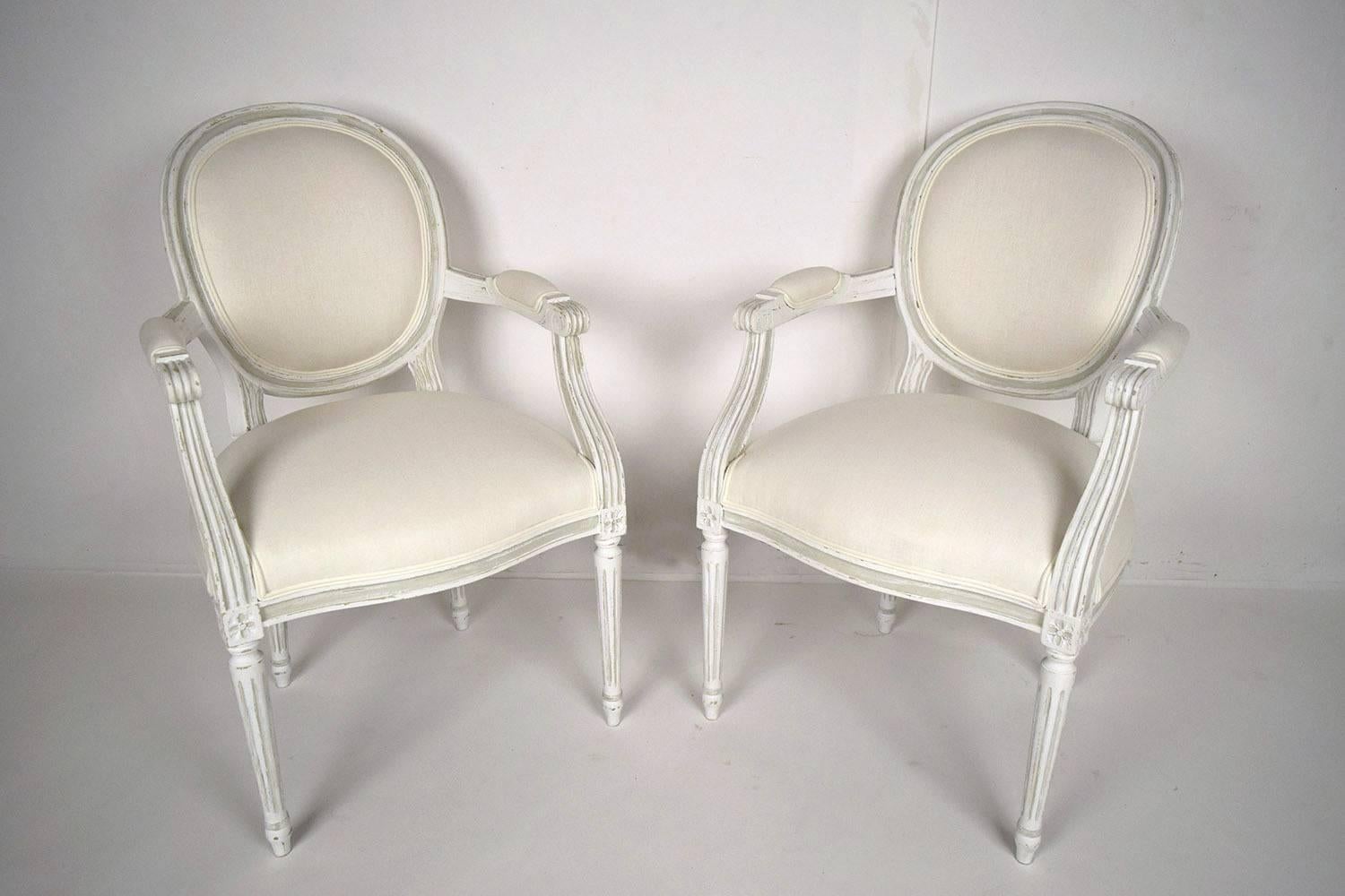 This pair of 1950s French Louis XIV-style hall chairs is made of solid carved maple wood frames with oval backs and features carved rosettes on the corners and fluted legs. The chairs are newly painted in an oyster color with a distressed finish.