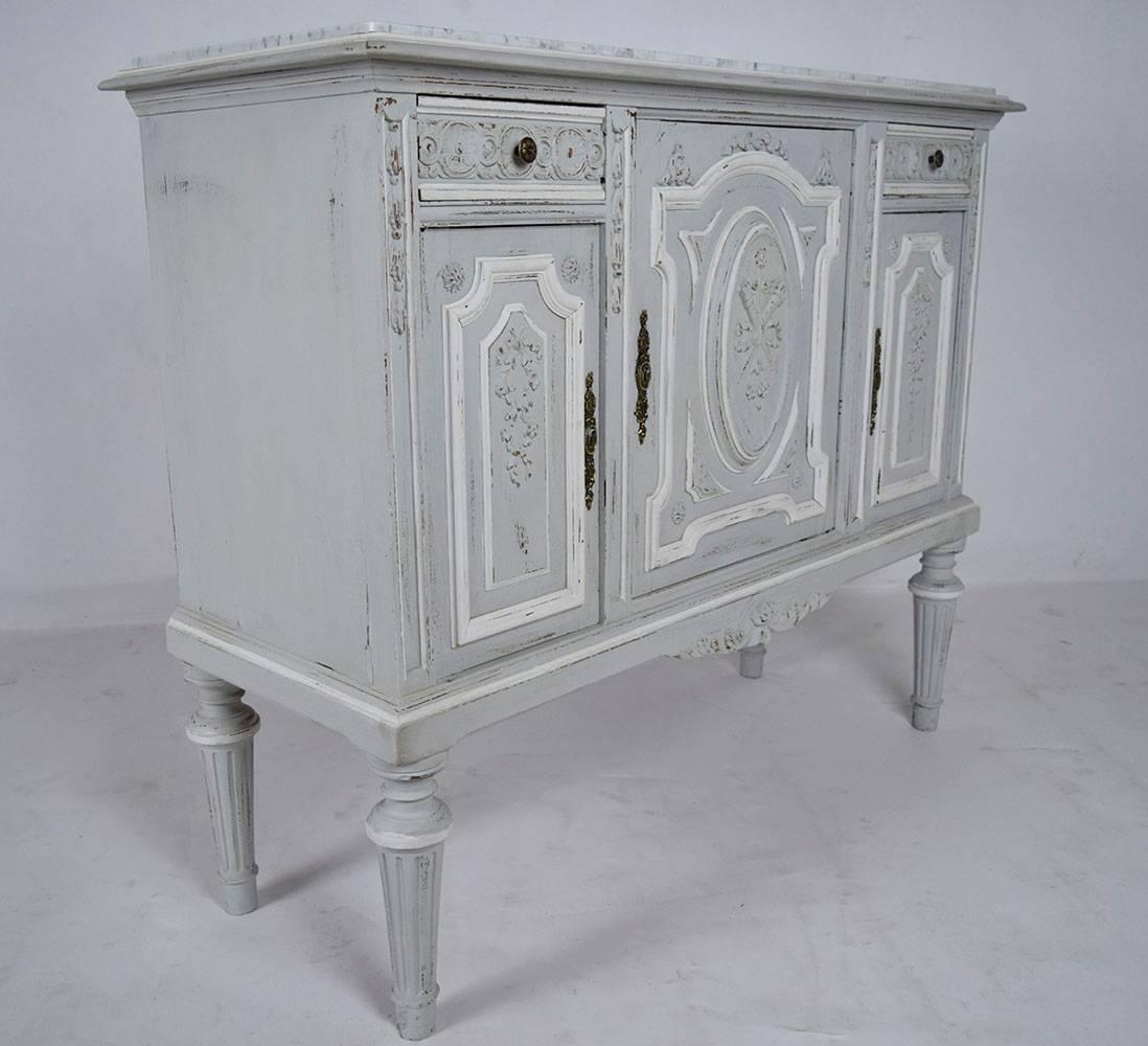 This 1880s French Louis XVI style server is made of walnut wood that has been painted in a pale grey and off white color combination with a distressed finish. On top of the server is an elegant white and grey marble slab. The facade of the server