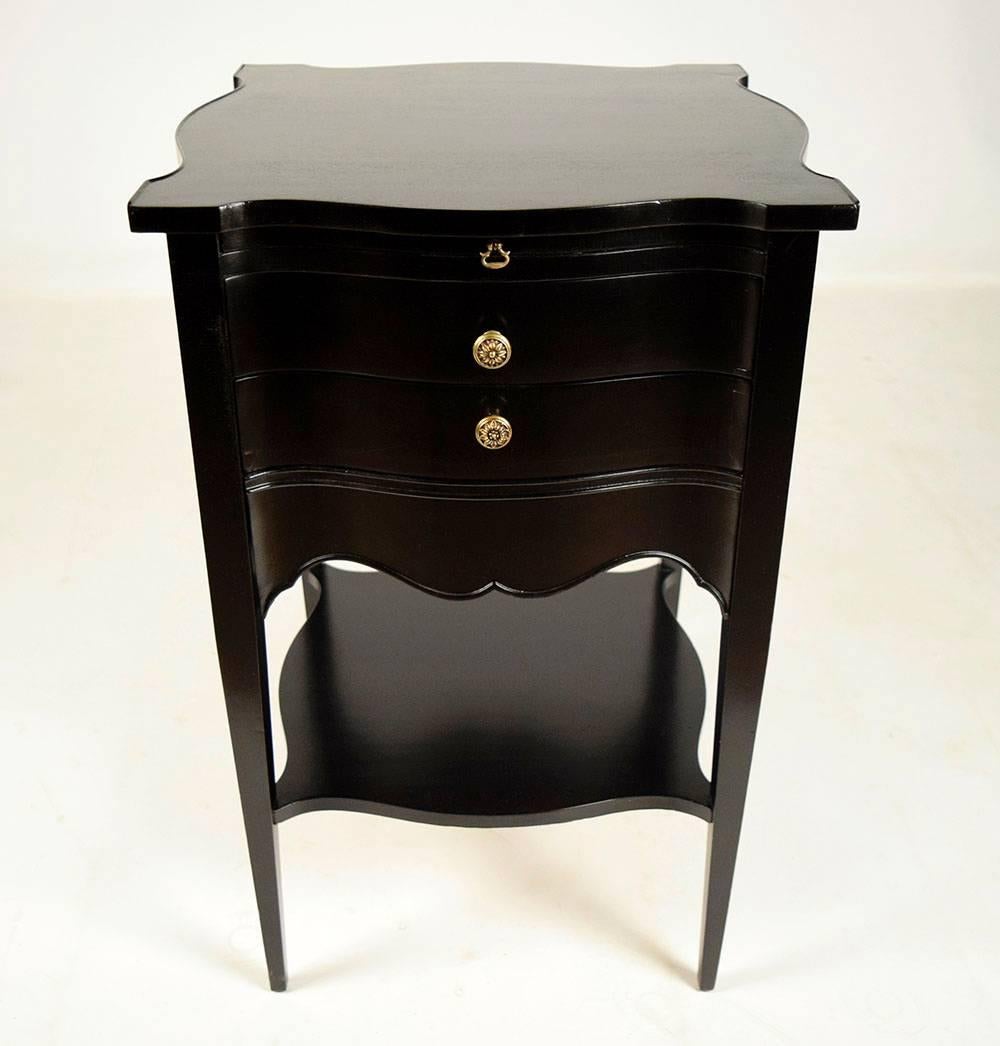 This pair of 1950s vintage side tables is designed by John Stuart and is made from mahogany wood. The side tables feature a beautiful black color ebonized finish. Each side table has three drawers with a serpentine front. The top two drawers have