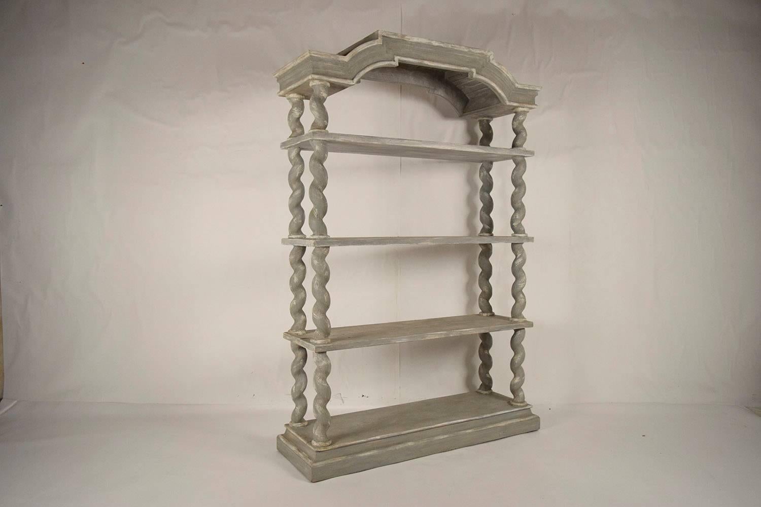 This large 1970s four-tier etagere or bookshelf is made of solid wood and is recently painted in a grey and oyster color combination with a distressed finish. The elegant pediment on top is supported by thick twisted supports and ha three thick