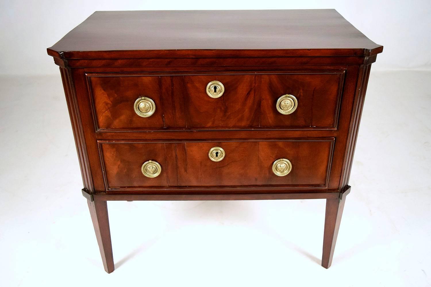 This 1910s French Empire-style chest is made from mahogany wood finished in a beautiful dark mahogany color stain finish. The chest features two full size drawers with delicate mouldings adorning their facades and two decorative brass drawer pulls