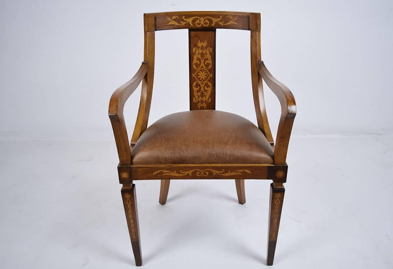 This 1900s antique English Regency-style armchair is made of wood that has been finished in a light walnut color stain. The frame features a curved black with complimenting carved arms. Adoring the front of the chair frame is exquisite inlaid