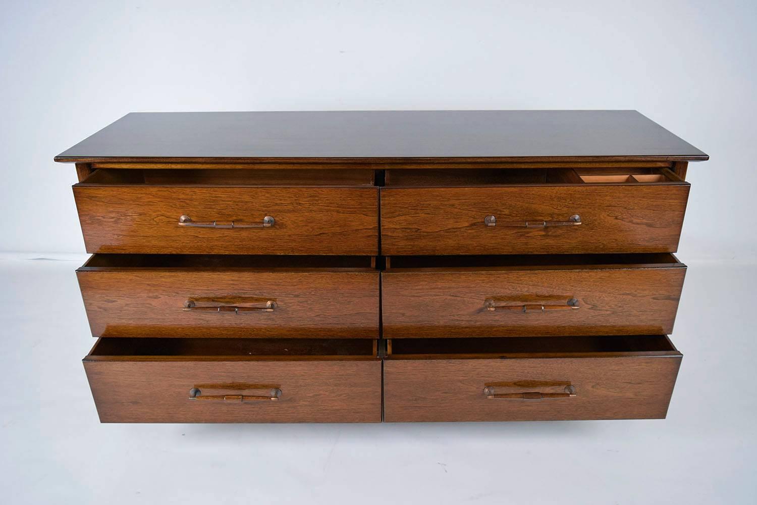 This 1960s Mid-Century Modern style dresser is designed by American of Martinsville. The teakwood dresser is finished in a rich dark walnut color stain. The elegant dresser features six drawers that are adorned with wood and brass handles. The