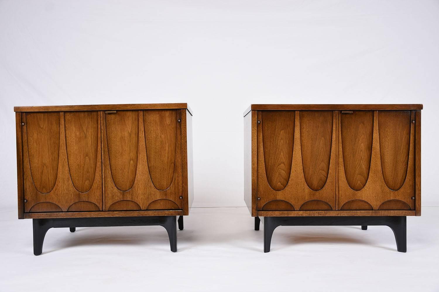 This 1960s vintage Mid-Century Modern-style pair of nightstands are made by Broyhill Brasilia. The nightstands are made from carved walnut wood that is finished in a rich walnut color stain. The facades of the doors feature the characteristic