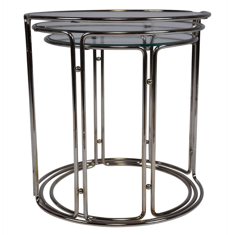 This 1960s Mid-Century Modern style set of three nesting tables is strikingly elegant. The tables feature two simple half circle chrome frames that join together at their vertical legs. The tables have circular glass tops. These nesting tables are