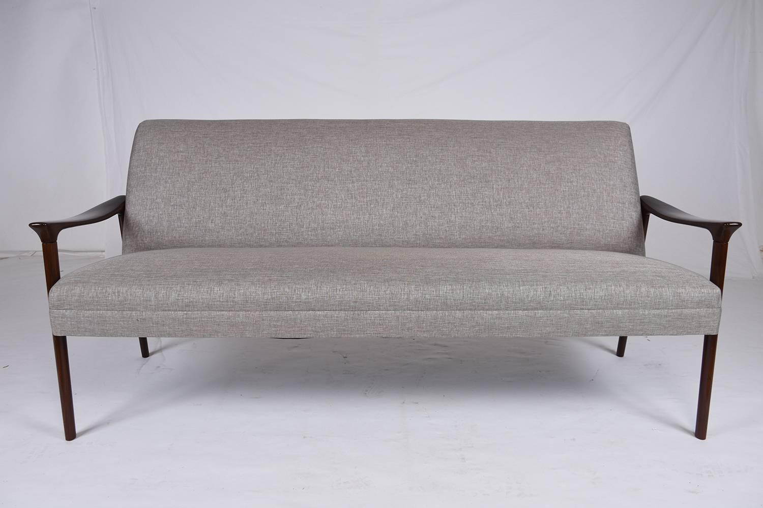 This 1960s vintage Danish Mid-Century Modern-style sofa features a teakwood frame that has been stained in rich, dark walnut stain with a lacquered finish. The gentle curve of the carved armrest and legs are accentuated by the simple cushion on the