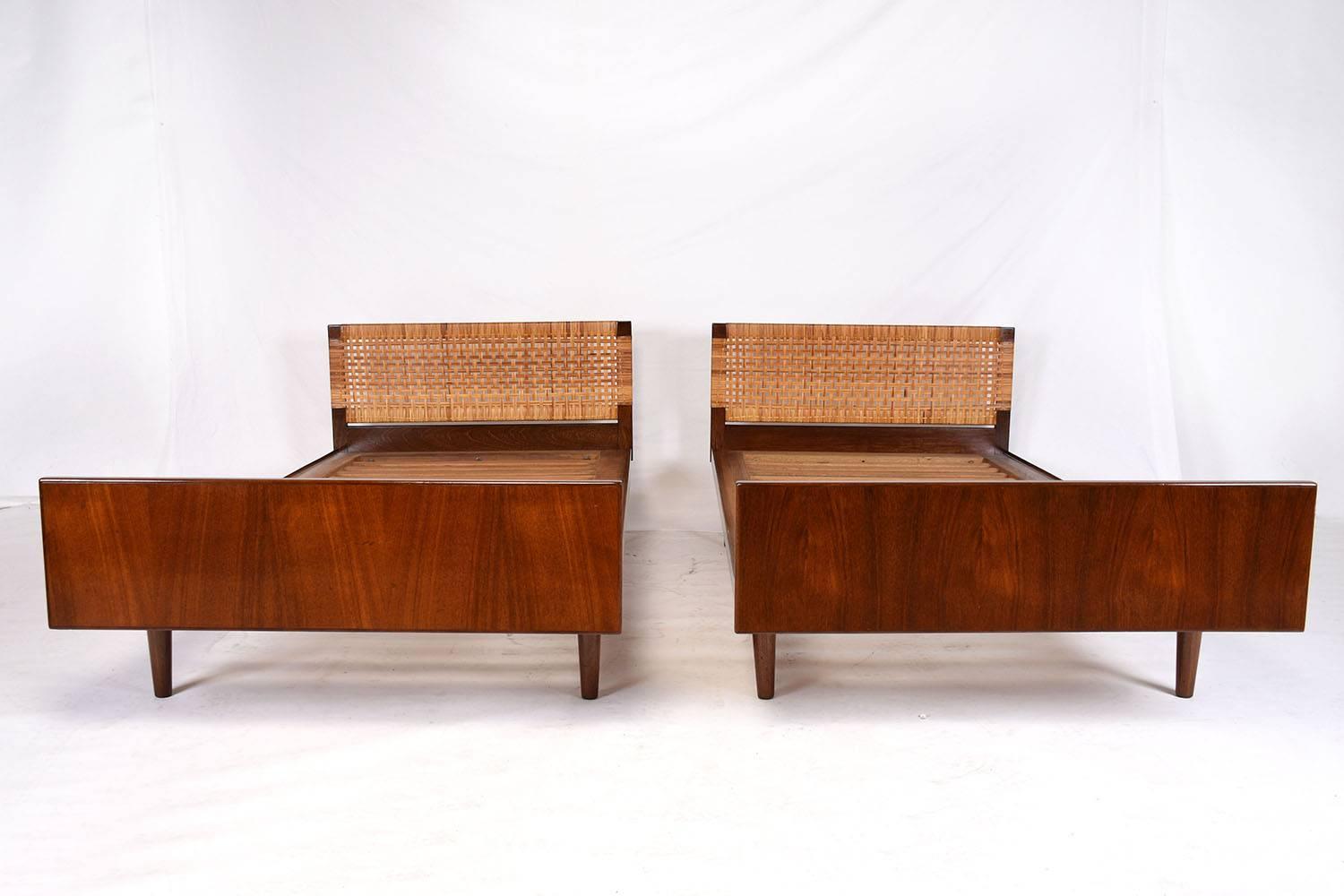 This 1960s Danish Mid-Century Modern-style pair of twin beds feature walnut wood frames in a Classic style. The frames have been stained in a rich walnut color with a lacquered finish. The headboard is uniquely decorated with caning details. The bed