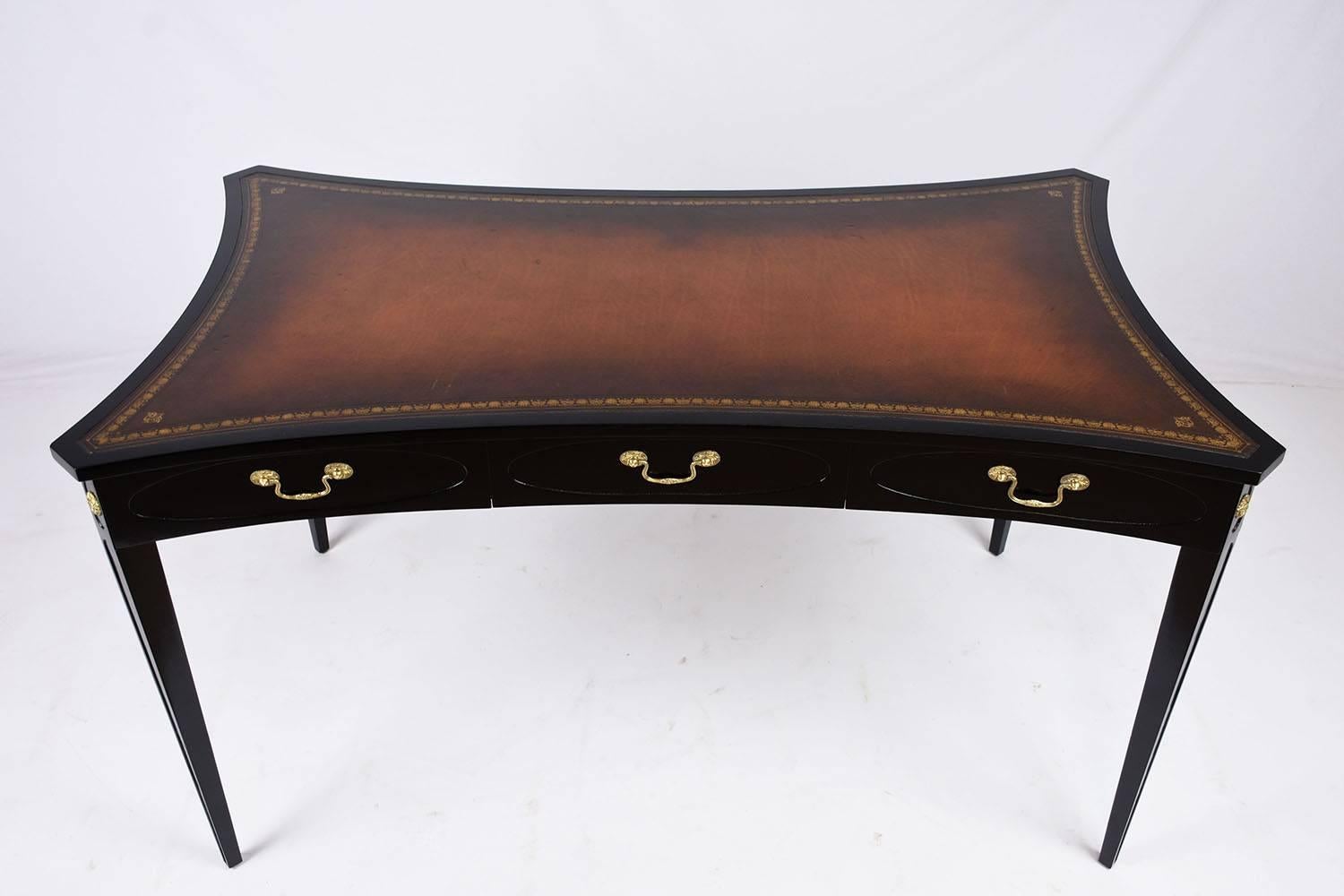 This 1980s vintage Regency-style desk is made of mahogany wood that has been stained in a rich black color with a lacquered finish. The top of the desk is uniquely shaped with an arc edge design. The simple design of the desk is accented by the