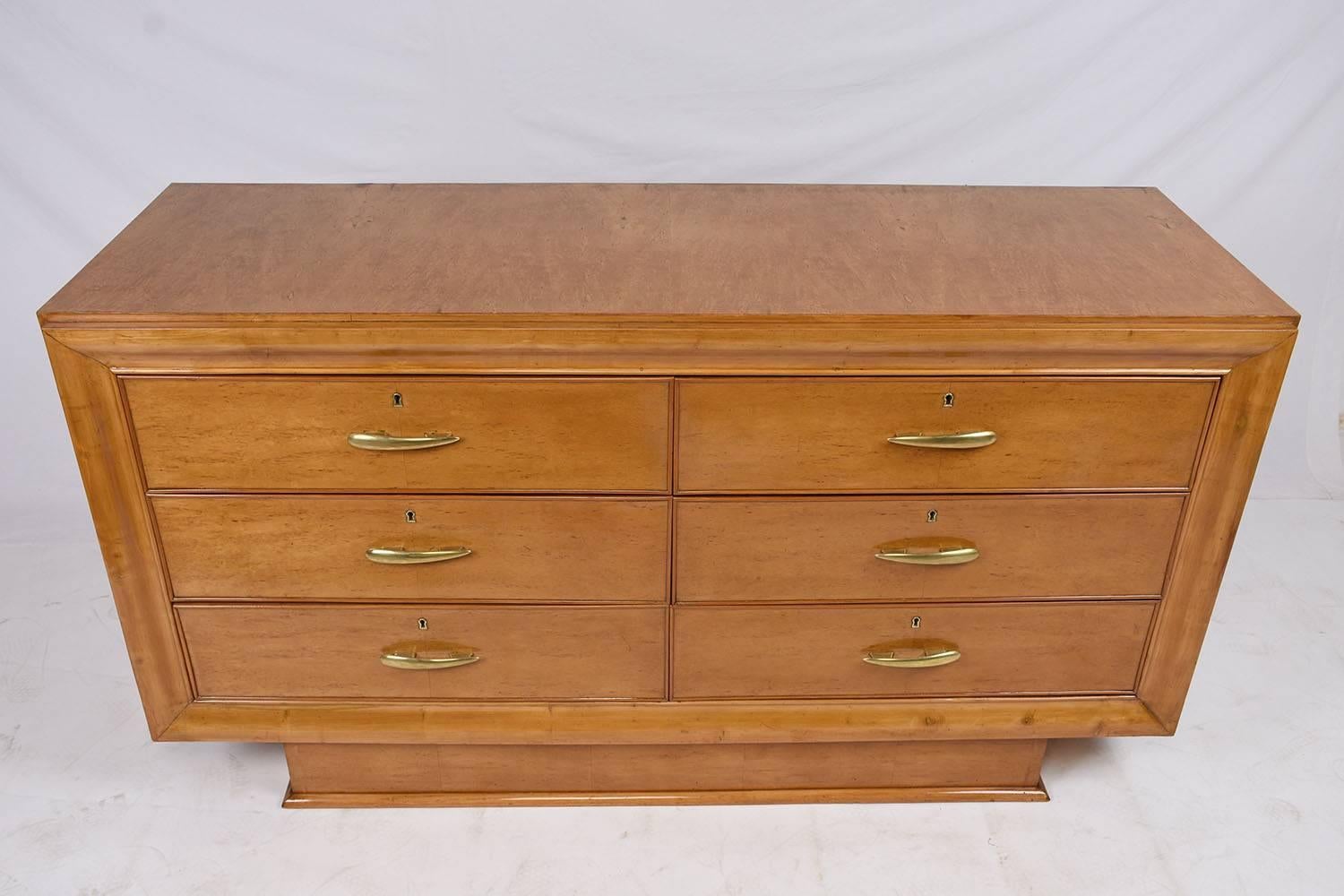 This 1930s Mid-Century Modern style chest of drawers is made from wood that has been adorned with beautiful birch wood veneers. The facade of this chest is defined by thick moulding details surrounding the six drawers. Each drawer has a brass handle