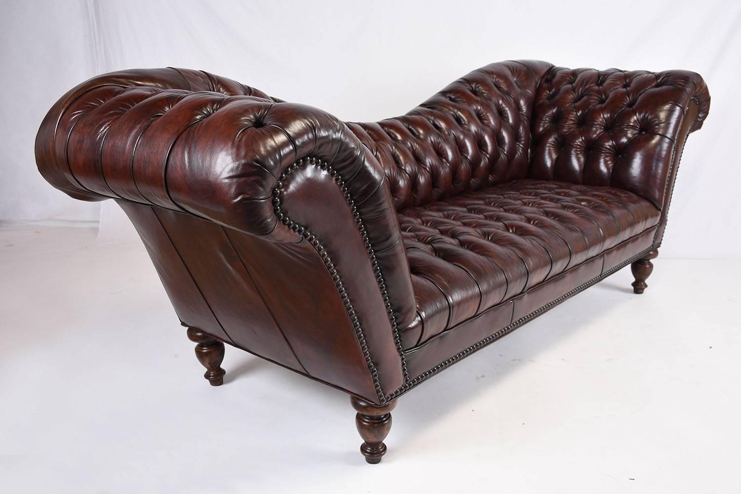 This 1970s vintage Hollywood Regency-style chesterfield sofa features a uniquely shaped swayed seat back. This comfortable sofa is upholstered in a dark brown colored leather on all sides of the sofa. The leather is adorned with tufted details on