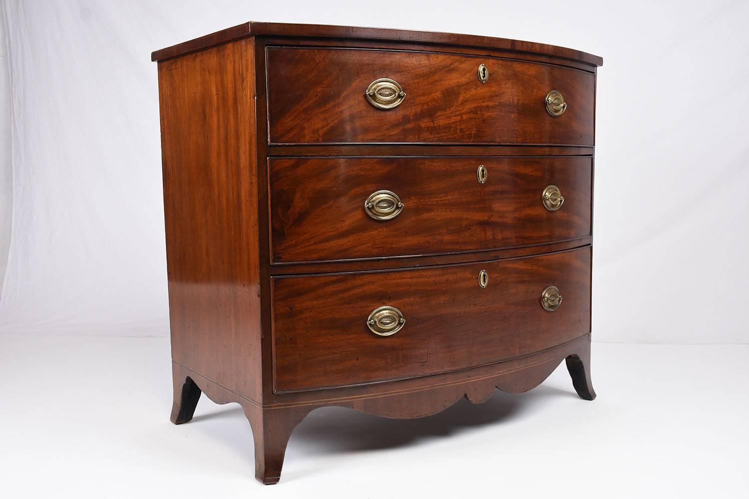 This 1870s antique George III style chest is made of mahogany wood with its original mahogany color stain finish. The top of the chest features a delicate inlaid design border. There are three drawers adorned with two decorative brass drawer pulls