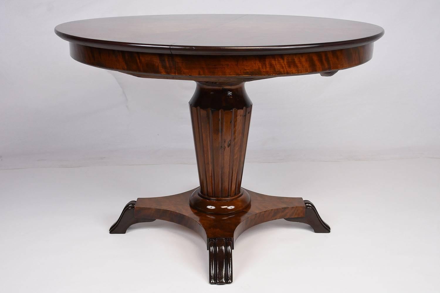This 1900s Antique Regency style side table is made of mahogany wood that features burl wood veneers stained in a rich mahogany color. The top of the table is adorned with geometric veneers that come together. The carved pedestal legs feature fluted