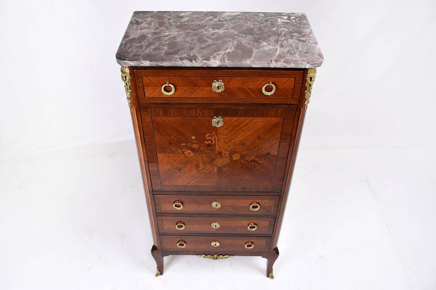 This 1890s Antique French Louis XVI-style secretaire is made from mahogany wood that has been stained in a rich medium wood tone color with marquetry details. Adorning the facade of the drop down door is an inlaid marquetry detail of a basket of
