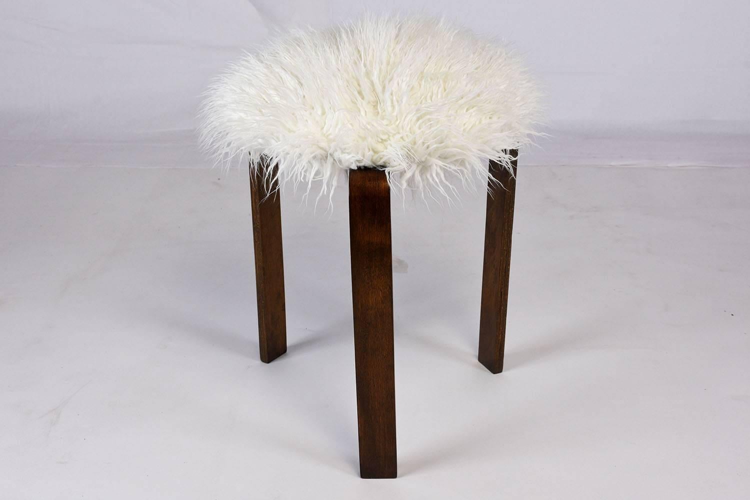 This 1960s Mid-Century Modern style stool is made of wood stained in a beautiful walnut finish. The three rectangular legs are accented by a comfortable seat. The seat has recently been professionally upholstered in a faux fur fabric. This unique