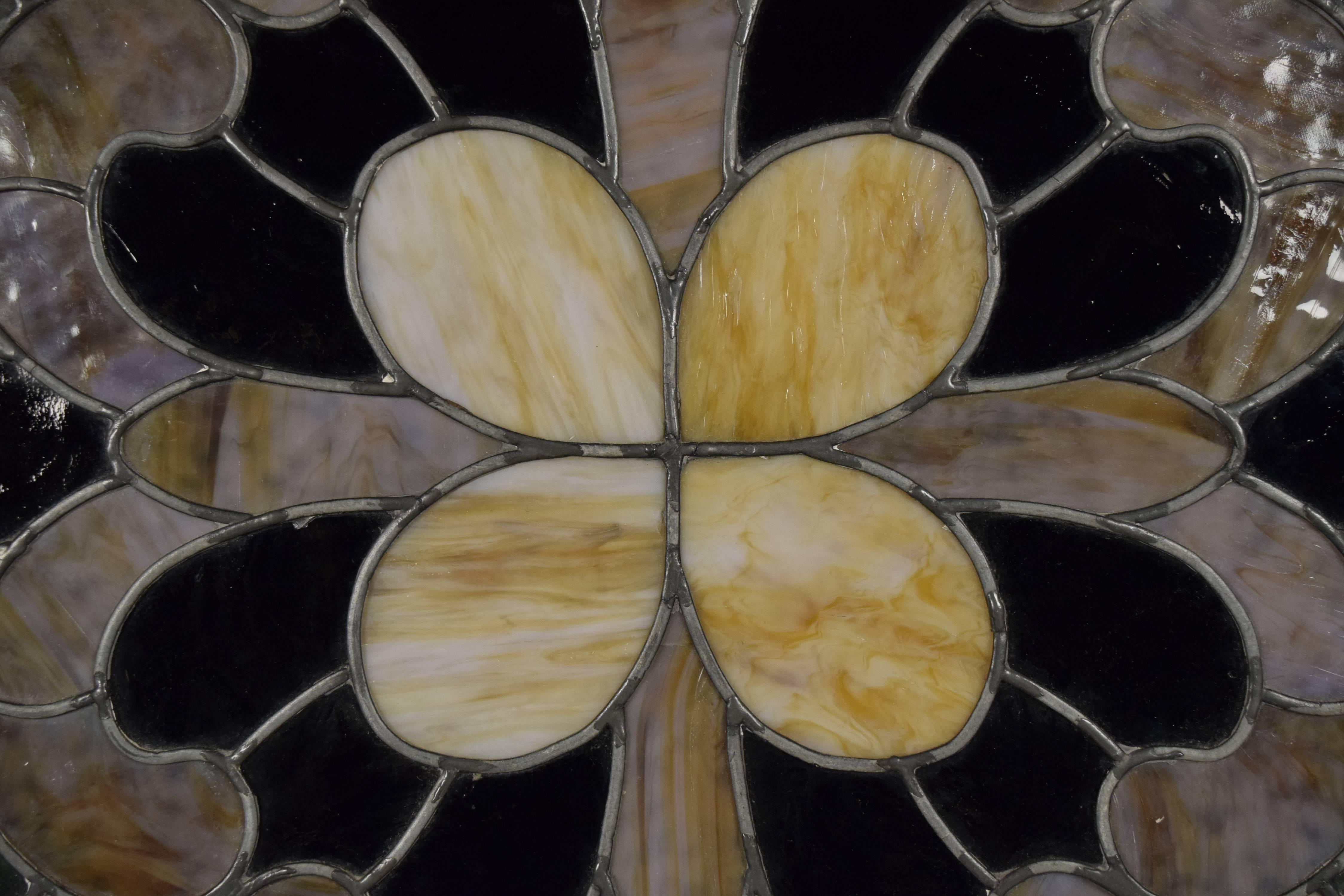 This 1900s antique round window features multicolored stained glass pieces. The stained glass comes together to form a beautiful floral design in red, yellow, and green tones. This piece can be used to adorn any home or office wall or