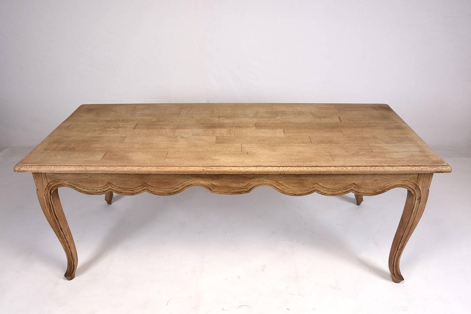 This 1970s French Provincial style dining table is made of oakwood with a intriguing bleached finish. This elegant table features carved serpentine legs with padded feet. Along the bottom edge of the table there is scallop trimming with carved