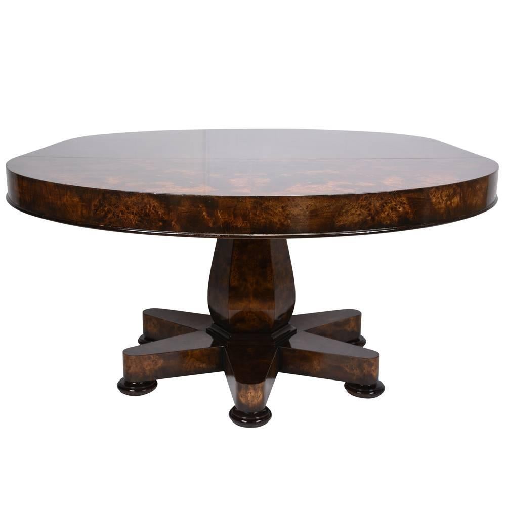 This 1970s Vintage Hollywood Regency-style dining or center table is made from solid wood covered in exotic burl wood veneers in a rich, dark walnut color stain and a lacquered finish. The pedestal legs are carved in a faceted design that correlates