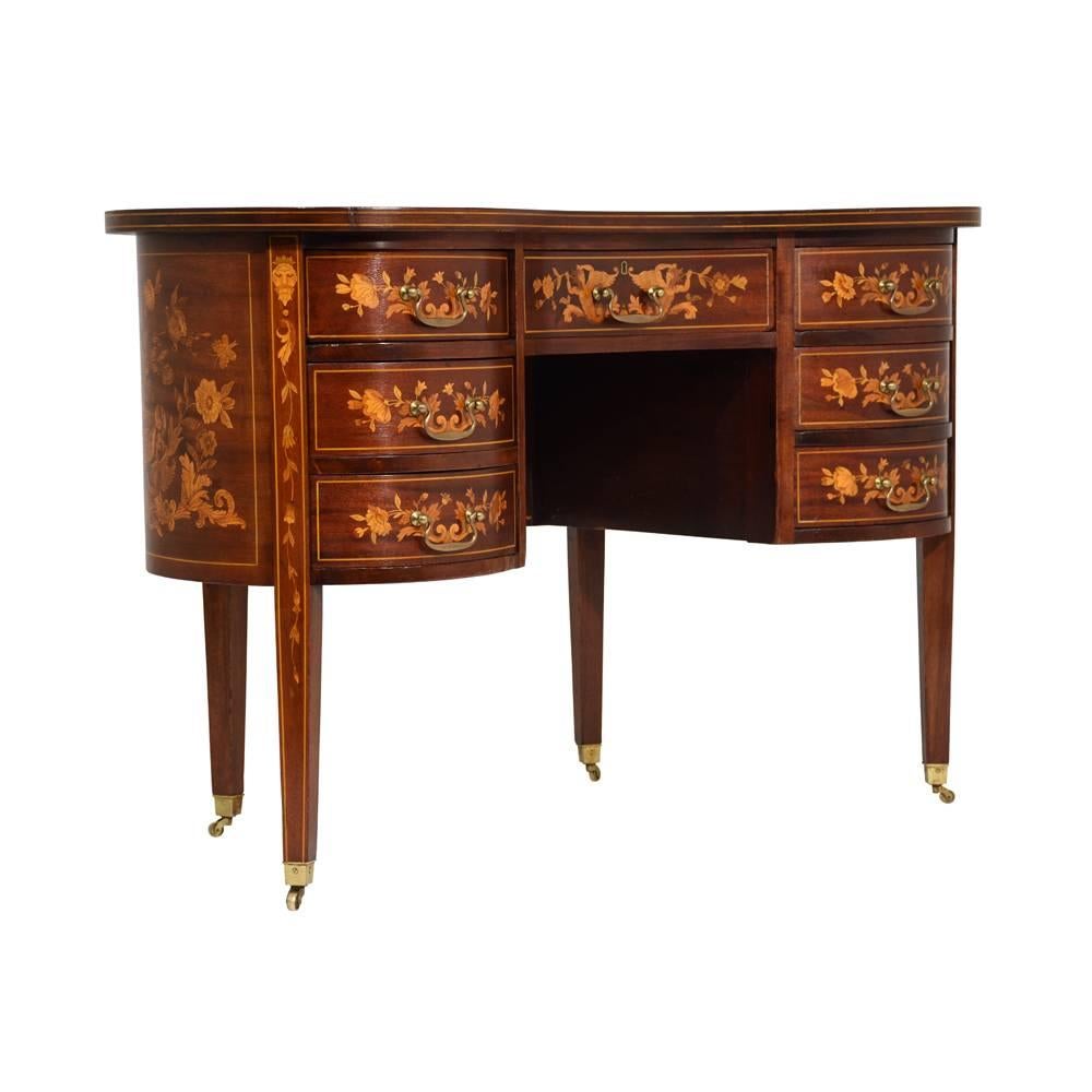 This 1900s antiques English Regency style kidney desk is made of wood stained in a mahogany color with a lacquered finish. Adorning the top, sides, front, and back are intricate marquetry designs of bouquets of flowers, vines, birds, acanthus