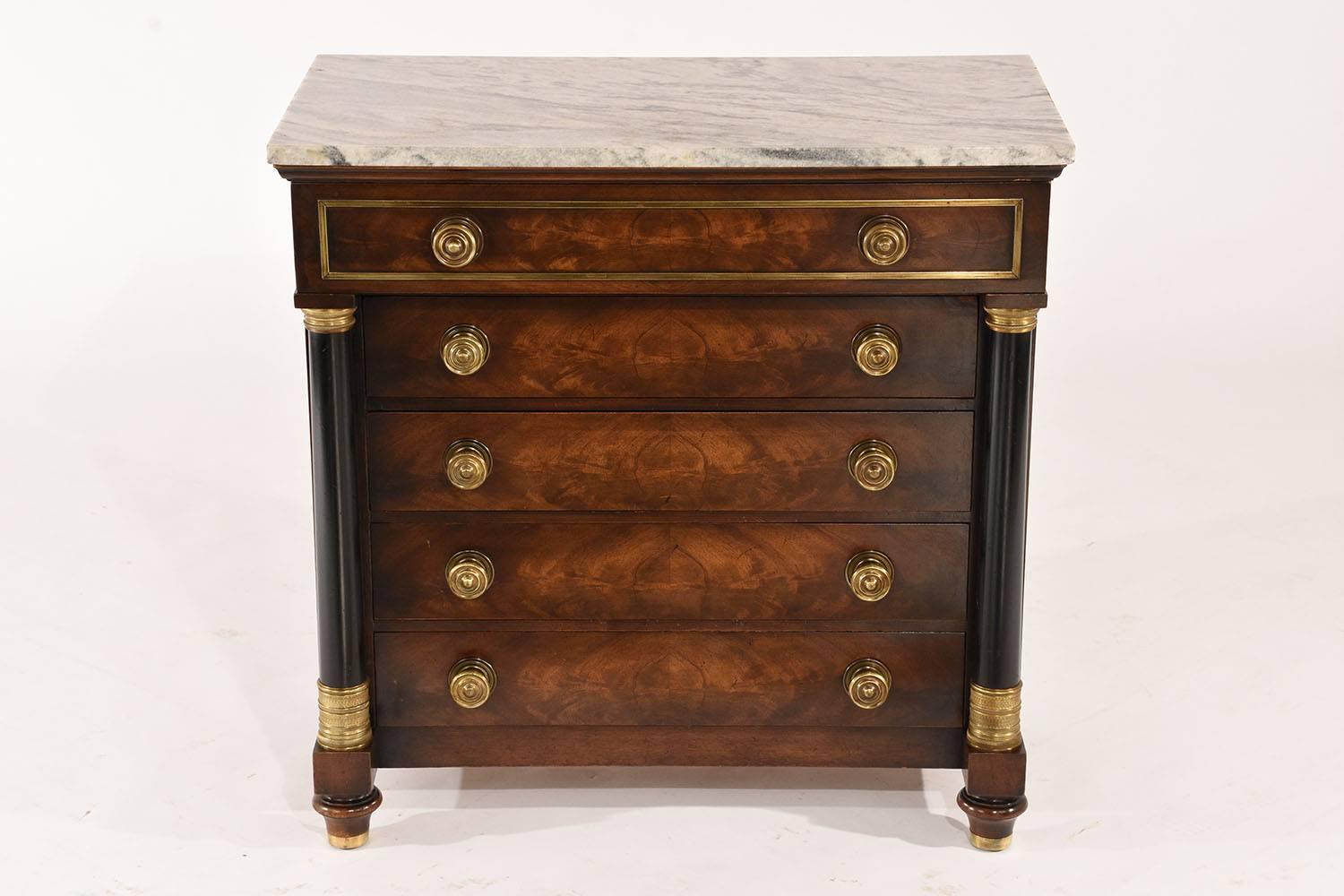 This 1970s Vintage Empire-style small chest of drawers or night stands are made of mahogany finished in a rich mahogany stain with ebonized details. The chest has five drawers with two decorative brass knobs each. On either side of the drawers are