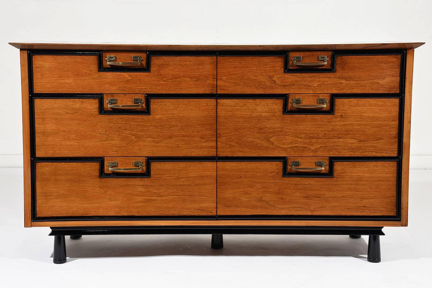 This 1960s Mid-Century Modern chest of drawers is made of walnut wood that has been stained in a rich walnut color with black accents and a lacquered finish. There are six drawers adorned with geometric black moulding accents and sleek brass