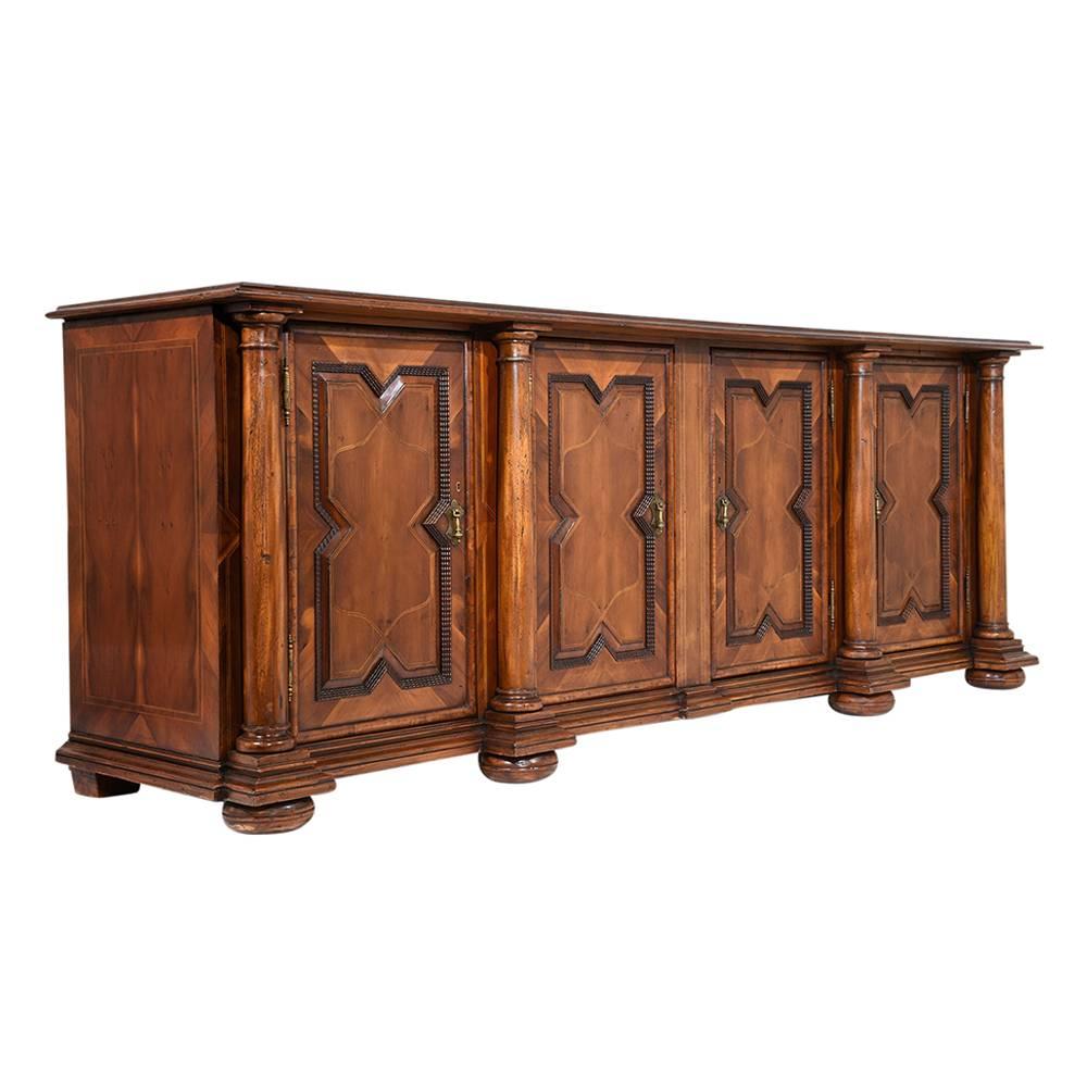 This 1970s Italian Baroque-style grand buffet is made of wood stained in a walnut color with a polished finish. The cabinet doors and sides are adorned with inlaid designs and carved moulding details. The doors are accented by carved columns and